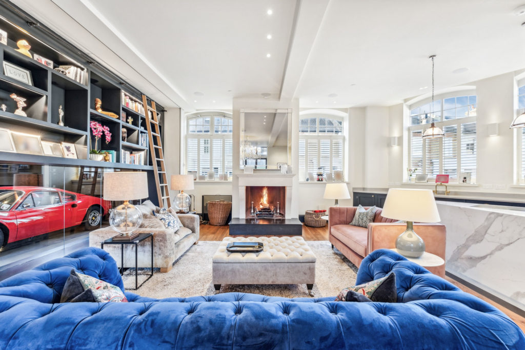 Living room with bright blue velvet sofa, black bookshelf, and Ferrari encased in glass