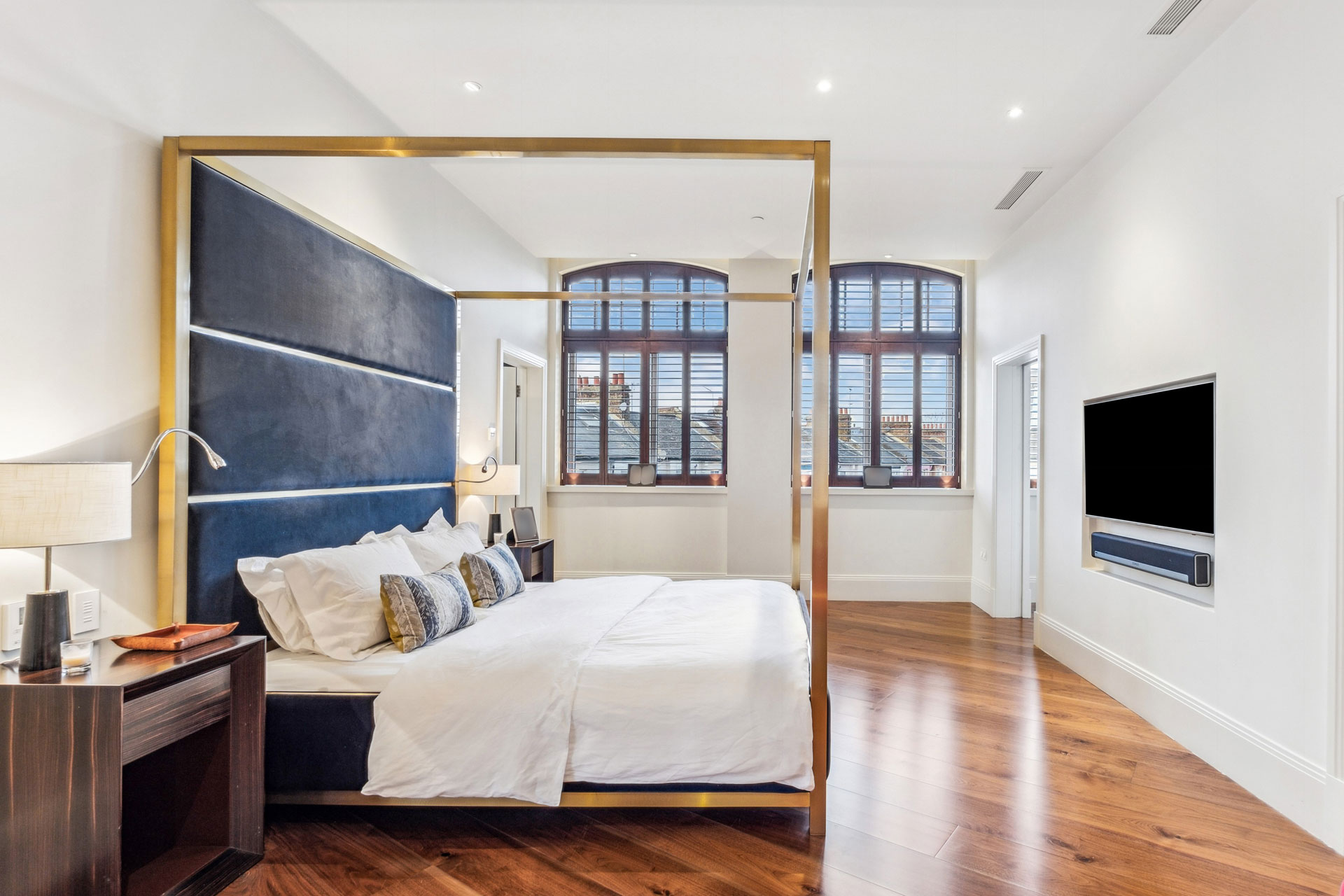 Bedroom with gold modern four poster bed, white linens and wooden floors