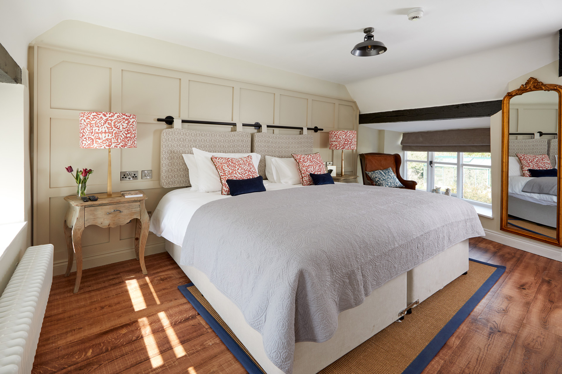 Bedroom with white linens, a grey and white striped bedspread and wooden floors.