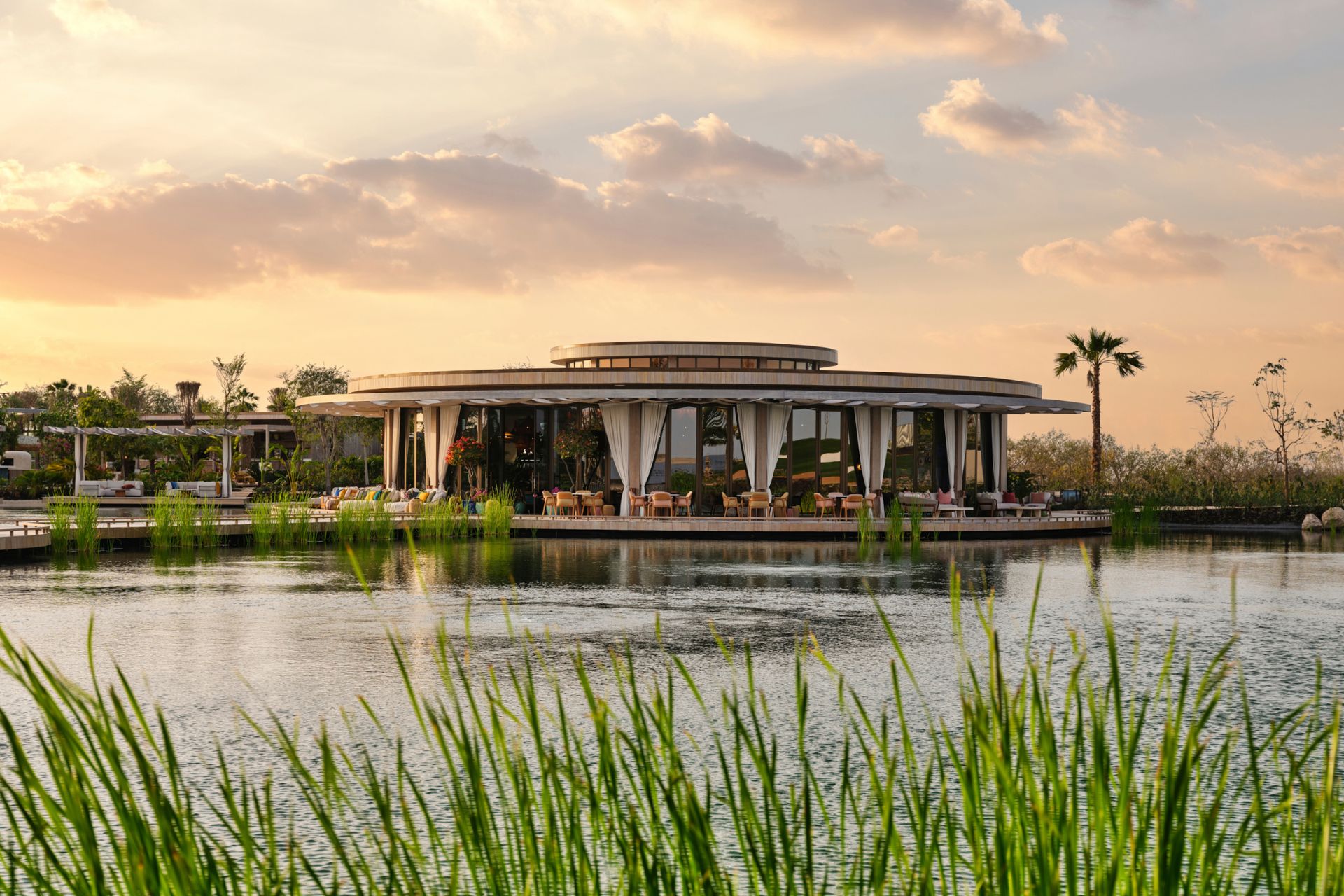 Exterior of round restaurant on the water in Dubai, with floor-to-ceiling windows and wooden decking.