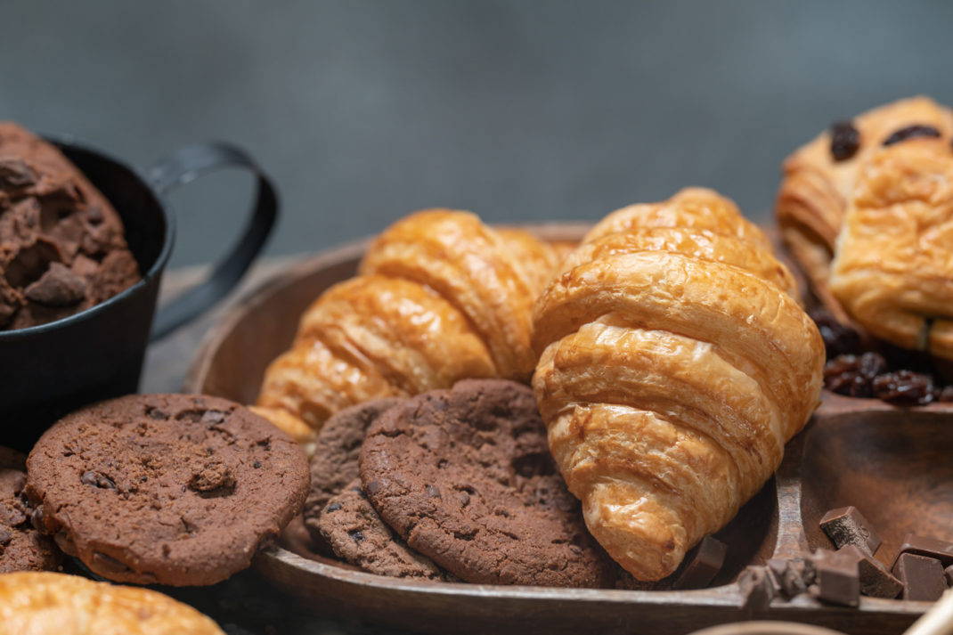 Closeup of Croissant with chocolate chip cookie on wooden plate.