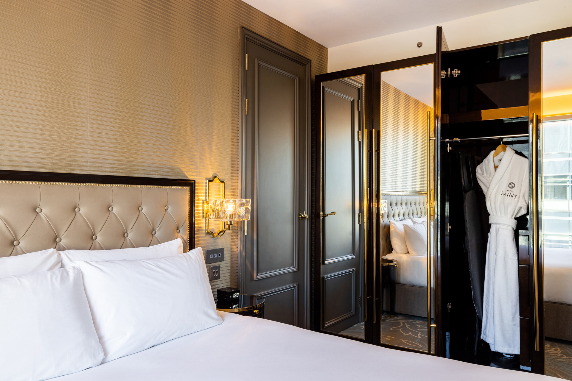 Hotel Saint bedroom with white linen and a white robe hanging in the wardrobe.