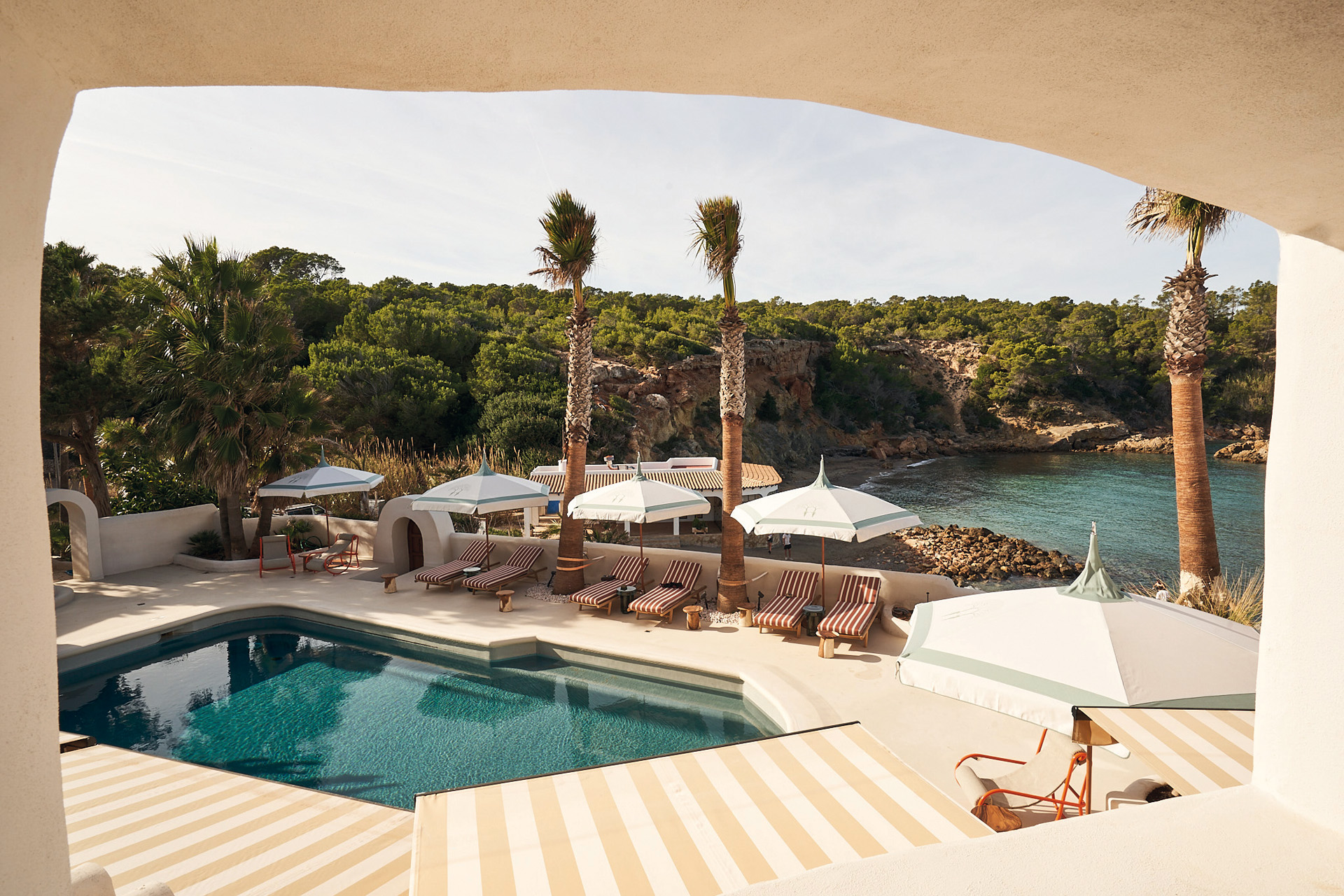 A pool with striped sun loungers beside the sea