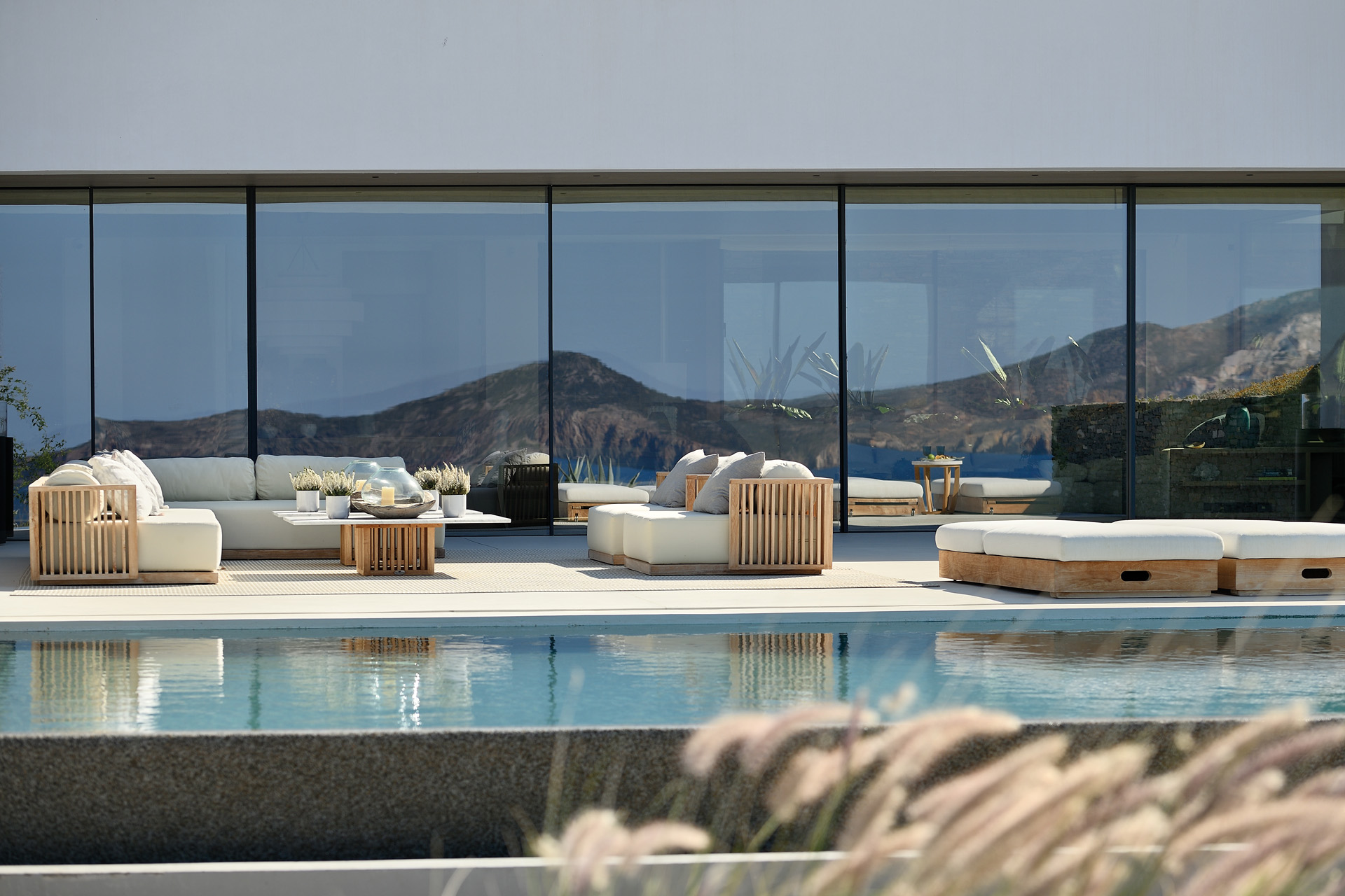 A luxury villa with a large glass wall overlooking the sea and mountains beyond
