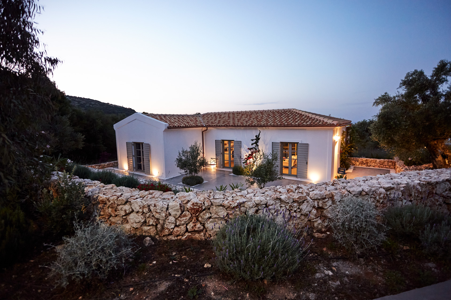 Exterior of Villa Allegra at night, with a terracotta roof and a stone wall surrounding it