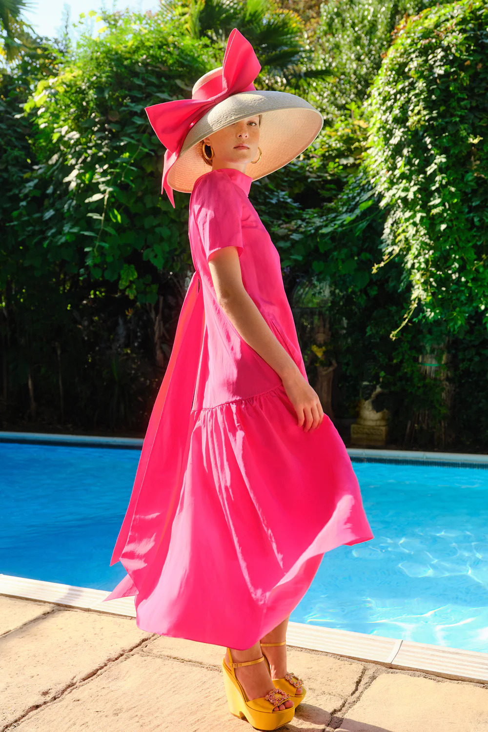 Woman in pink dress and straw hat by pool