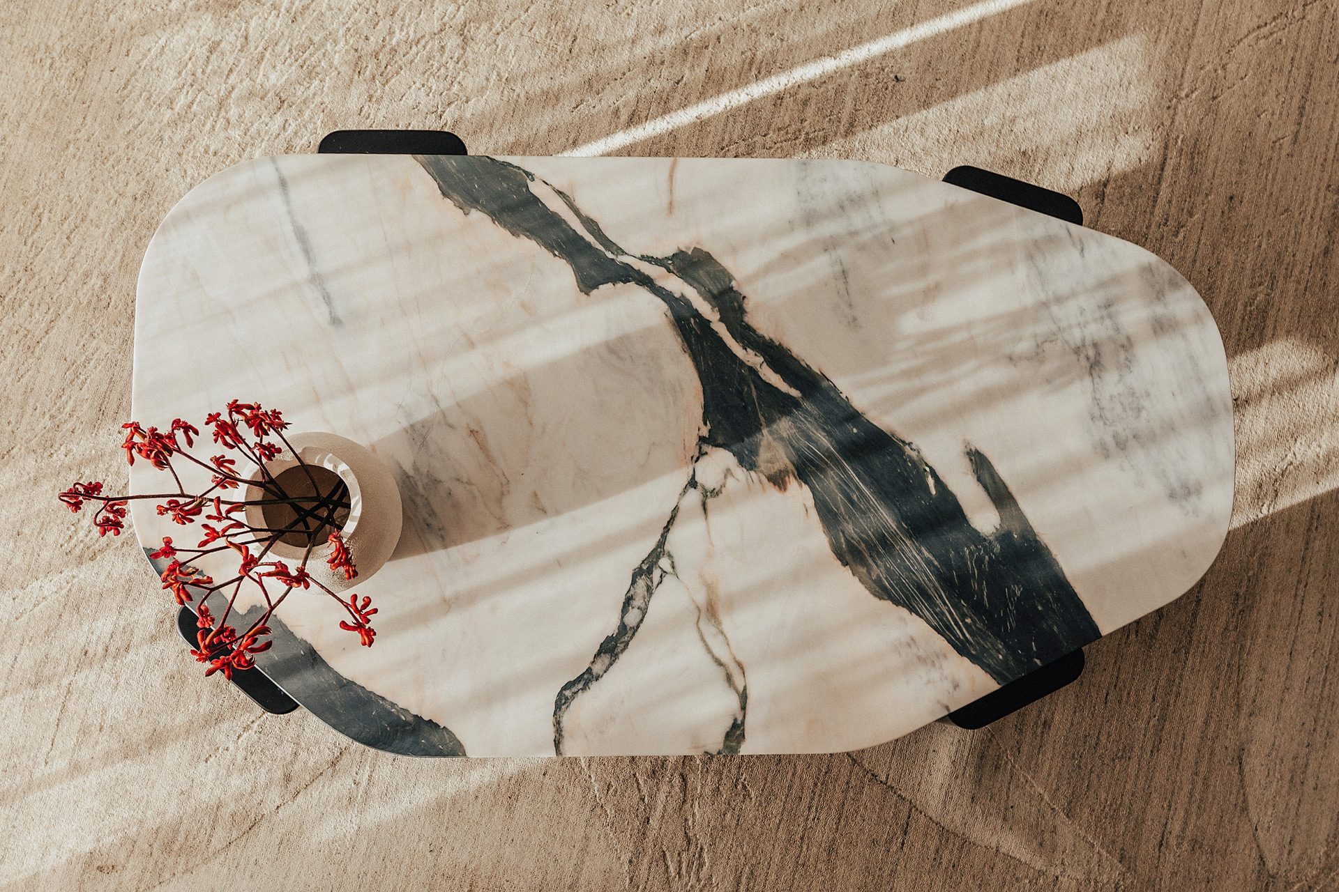 Aerial view of asymmetrical marble coffee table with a vase of pink flowers on top.