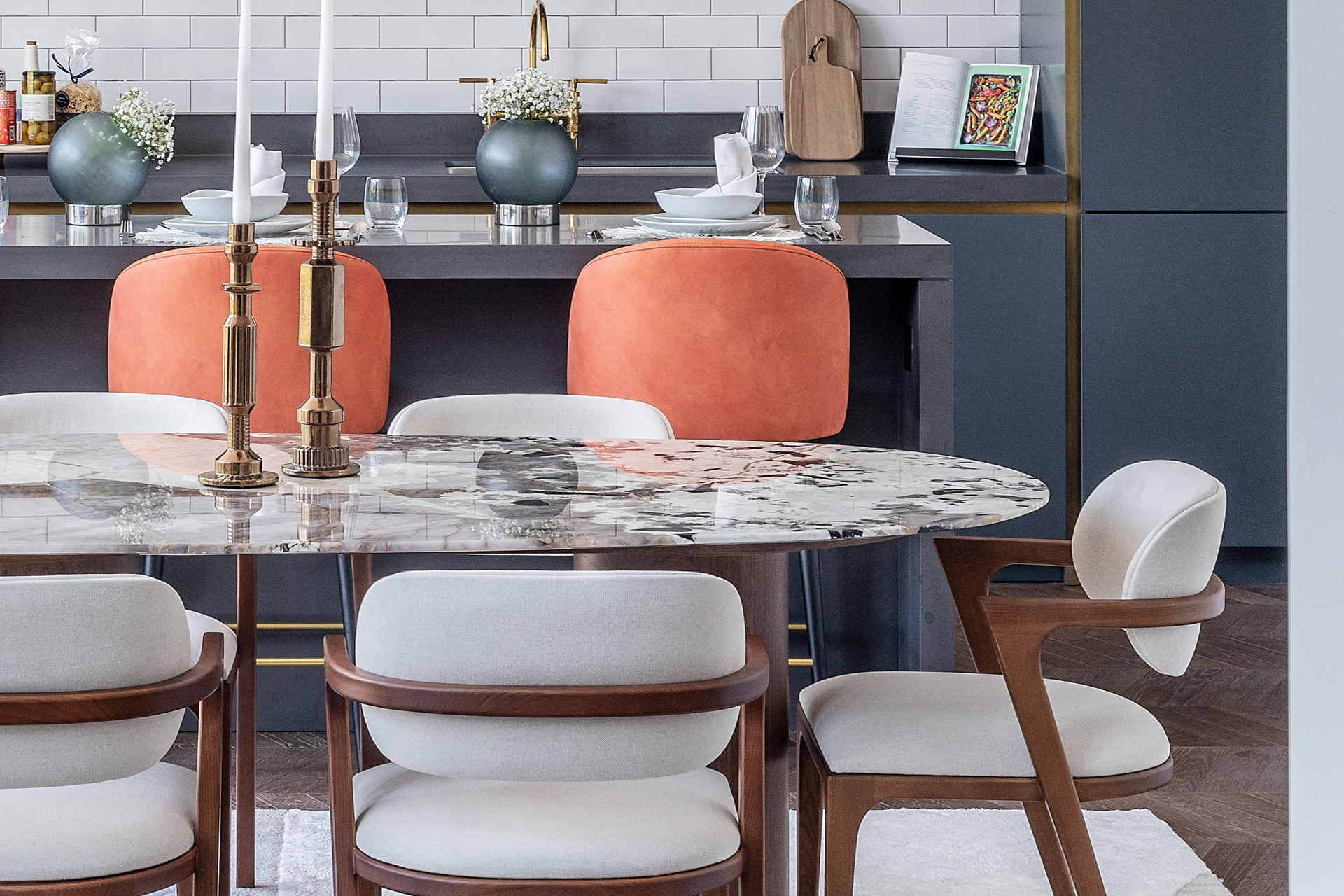 Marble-topped dining table surrounded by white chairs, in a navy blue kitchen.