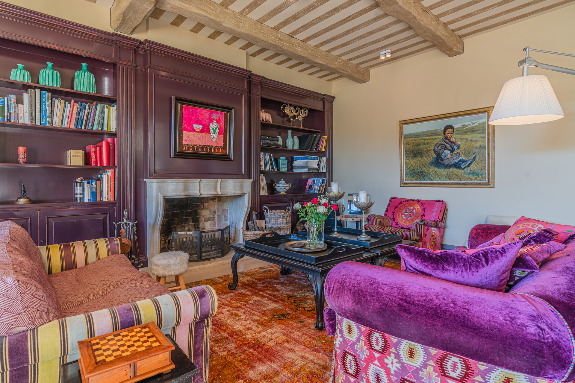 Living room with purple velvet sofas, a stripey brown armchair and purple bookshelves.