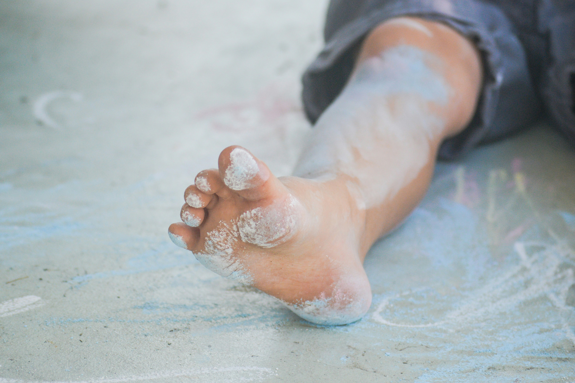 A child's foot covered in colourful dust from playing with chalk