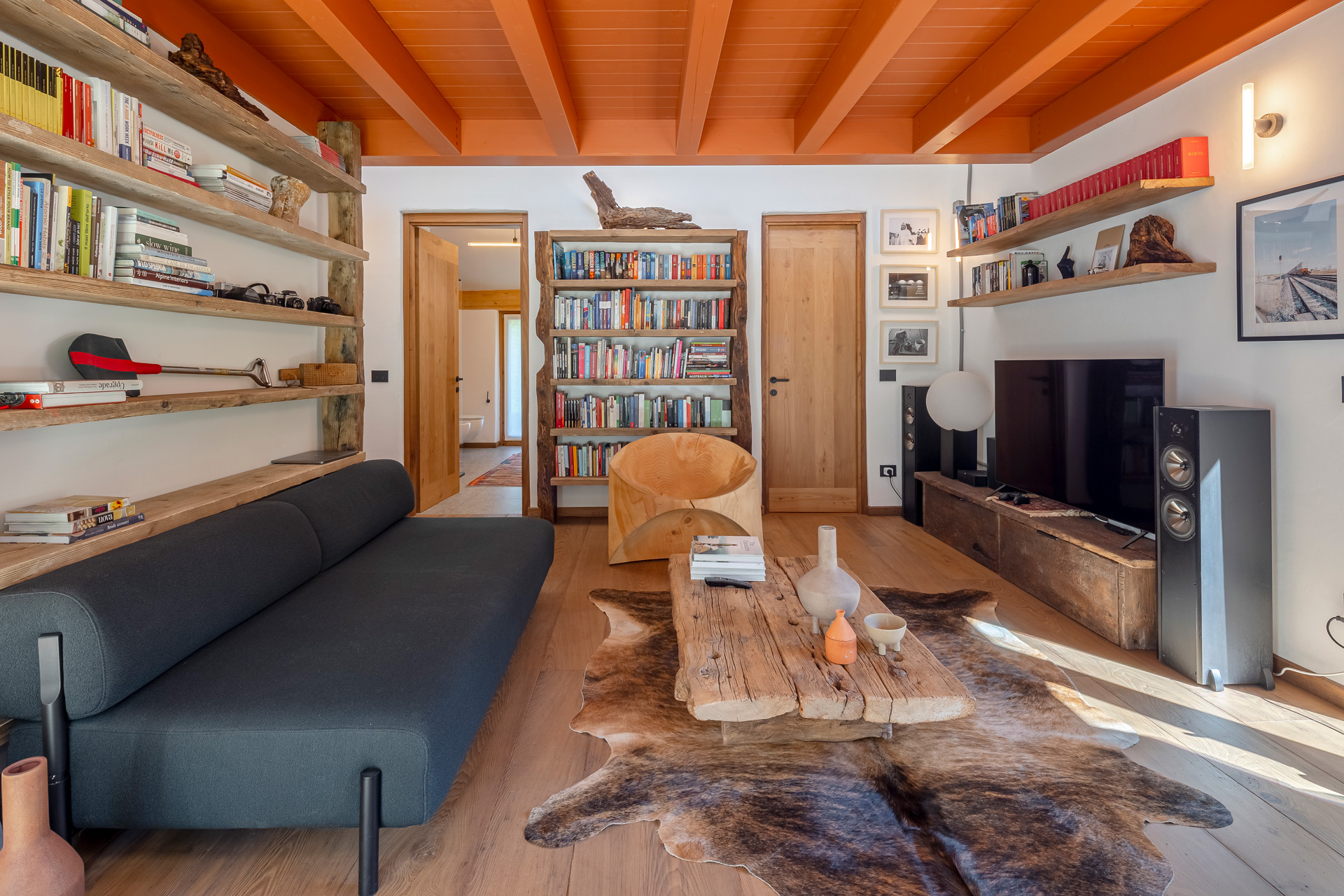 Living room with wooden ceiling beams, a grey modular sofa and an animal hide rug.