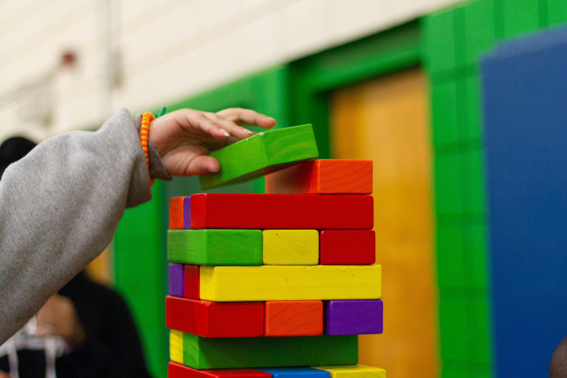 A child placing a colourful Jenga block onto a tower