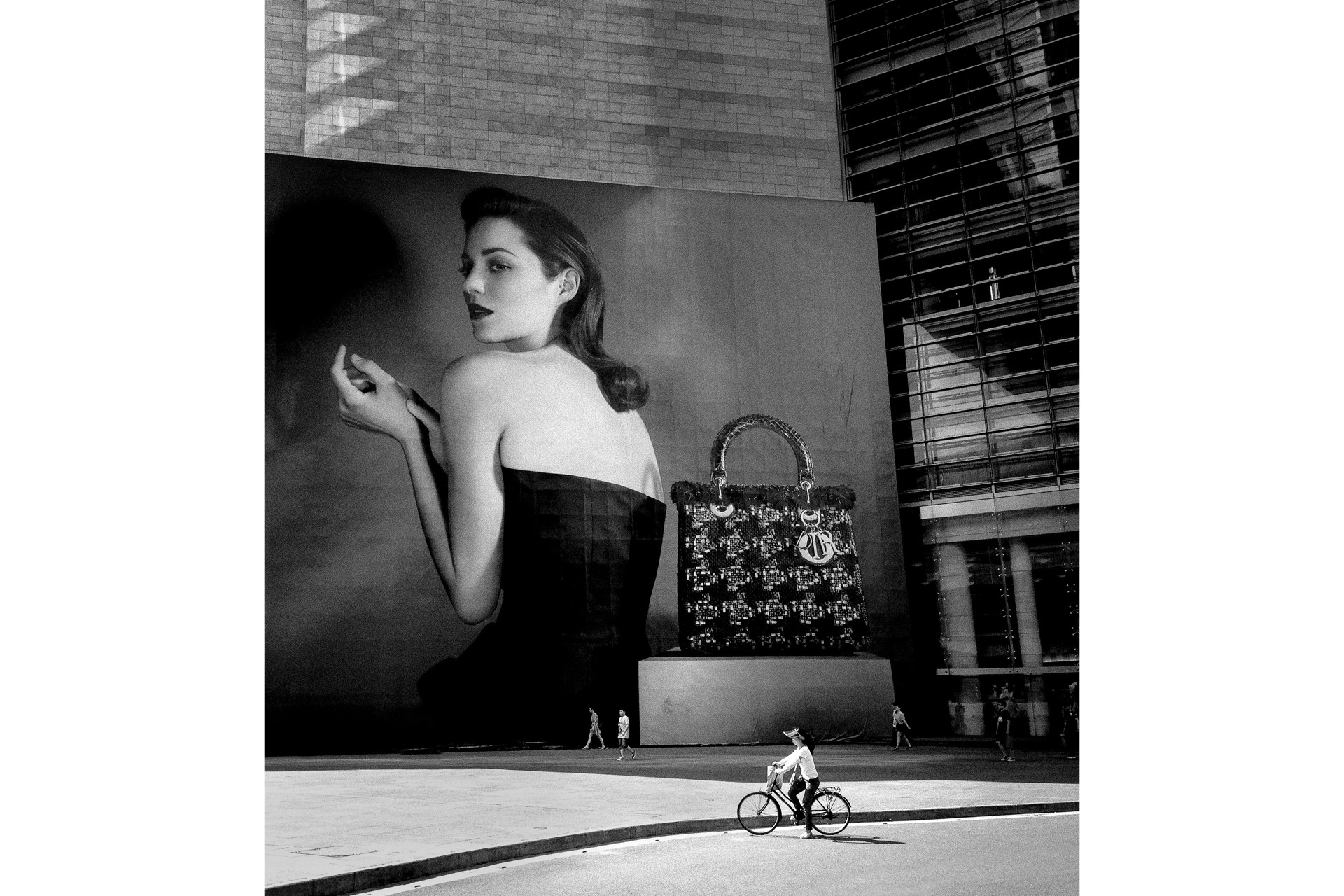 A large billboard of a woman, dwarfing a real woman on a bike