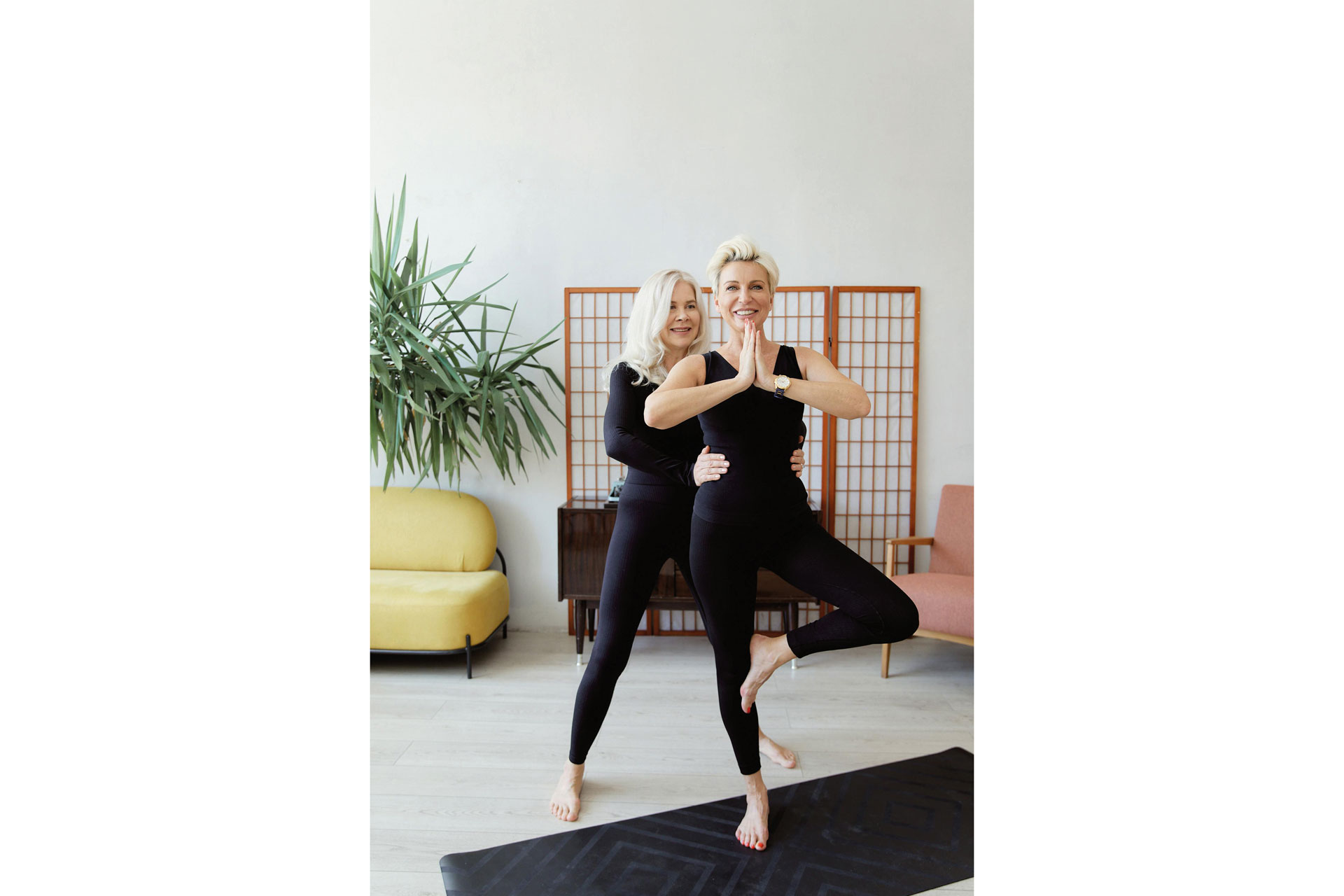 Woman doing a tree pose being helped by a trainer