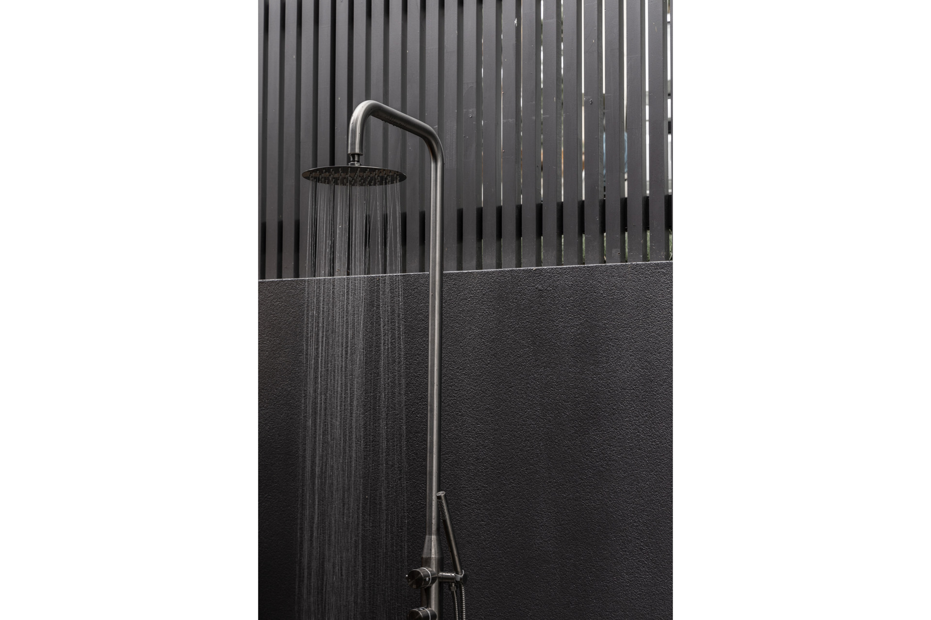An outdoor shower against a black wall