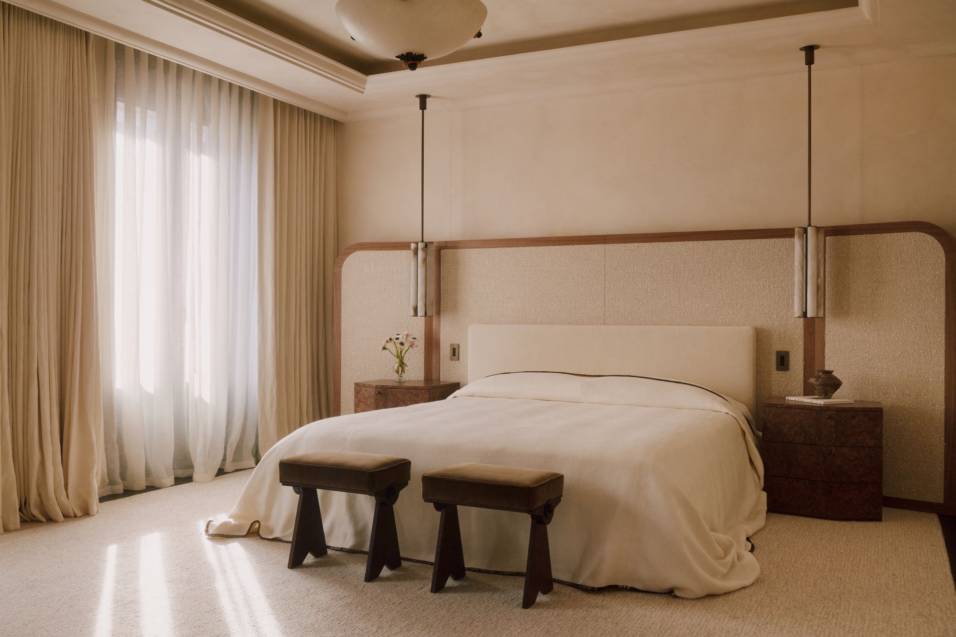 Master bedroom with white bed linen, a cream fabric headboard and two wooden stools.
