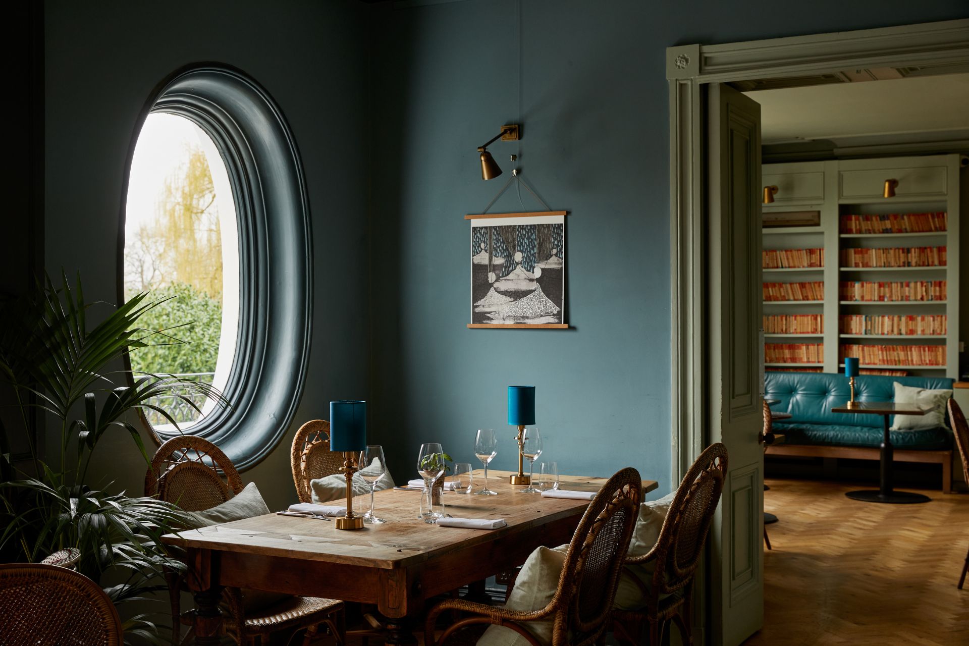 teal blue dining room with an oval-shaped window and wooden tables.