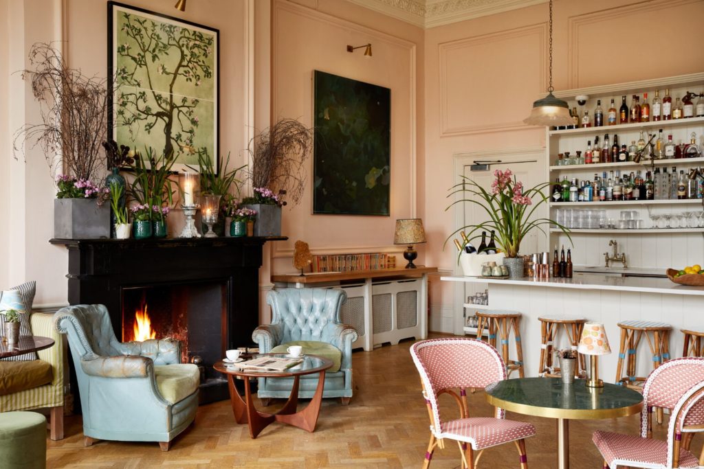 Drawing Room Bar at Bingham Riverhouse, featuring a large fireplace, blue armchairs, pink wicker seats and gold tables.