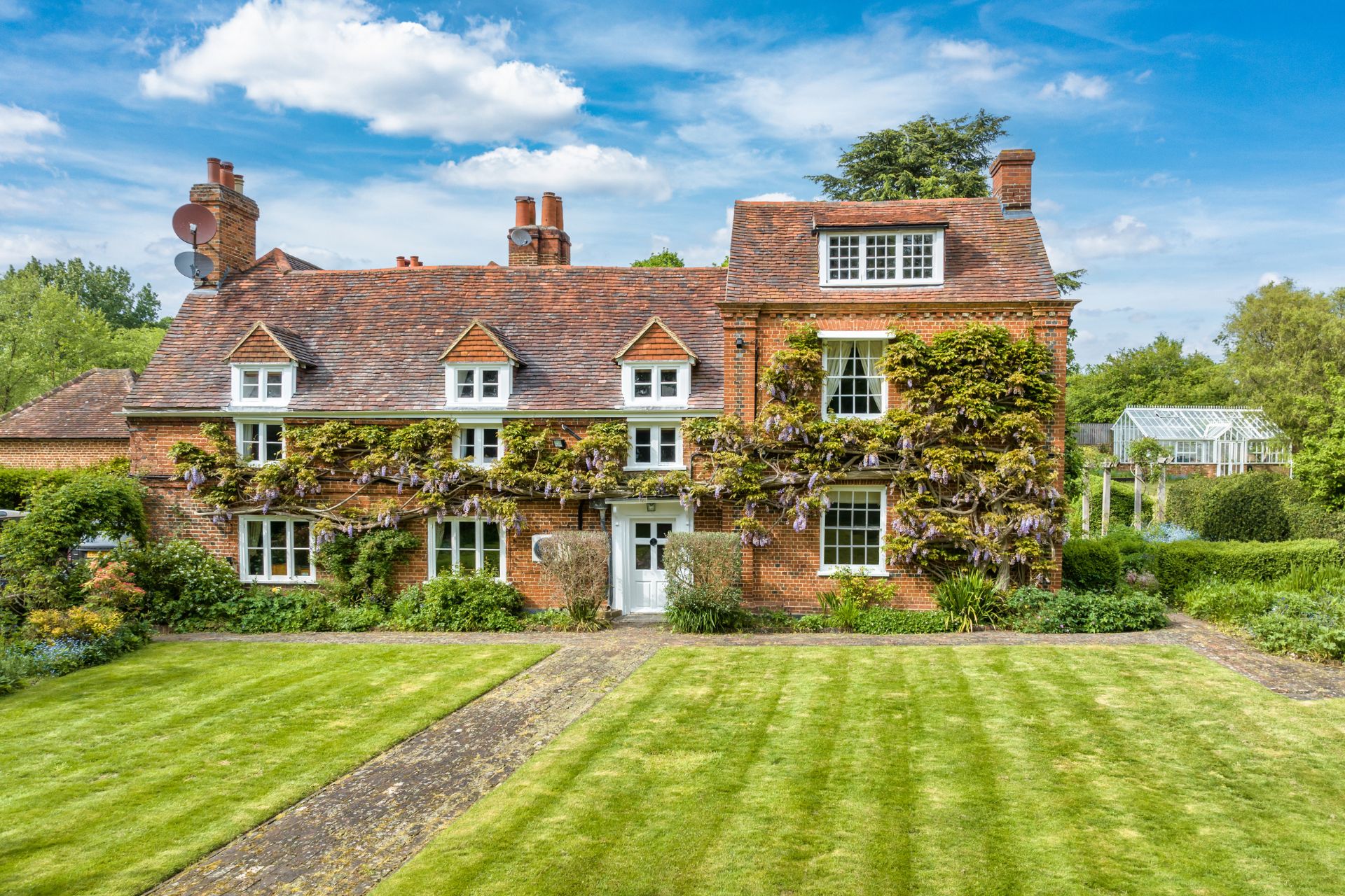 Red brick Surrey home with wisteria-clad facade and a front lawn.
