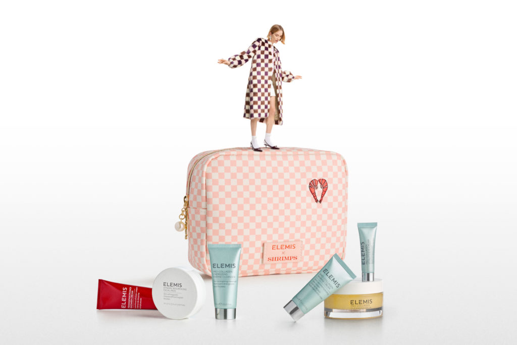 Tiny woman stood on washbag surrounded by beauty products
