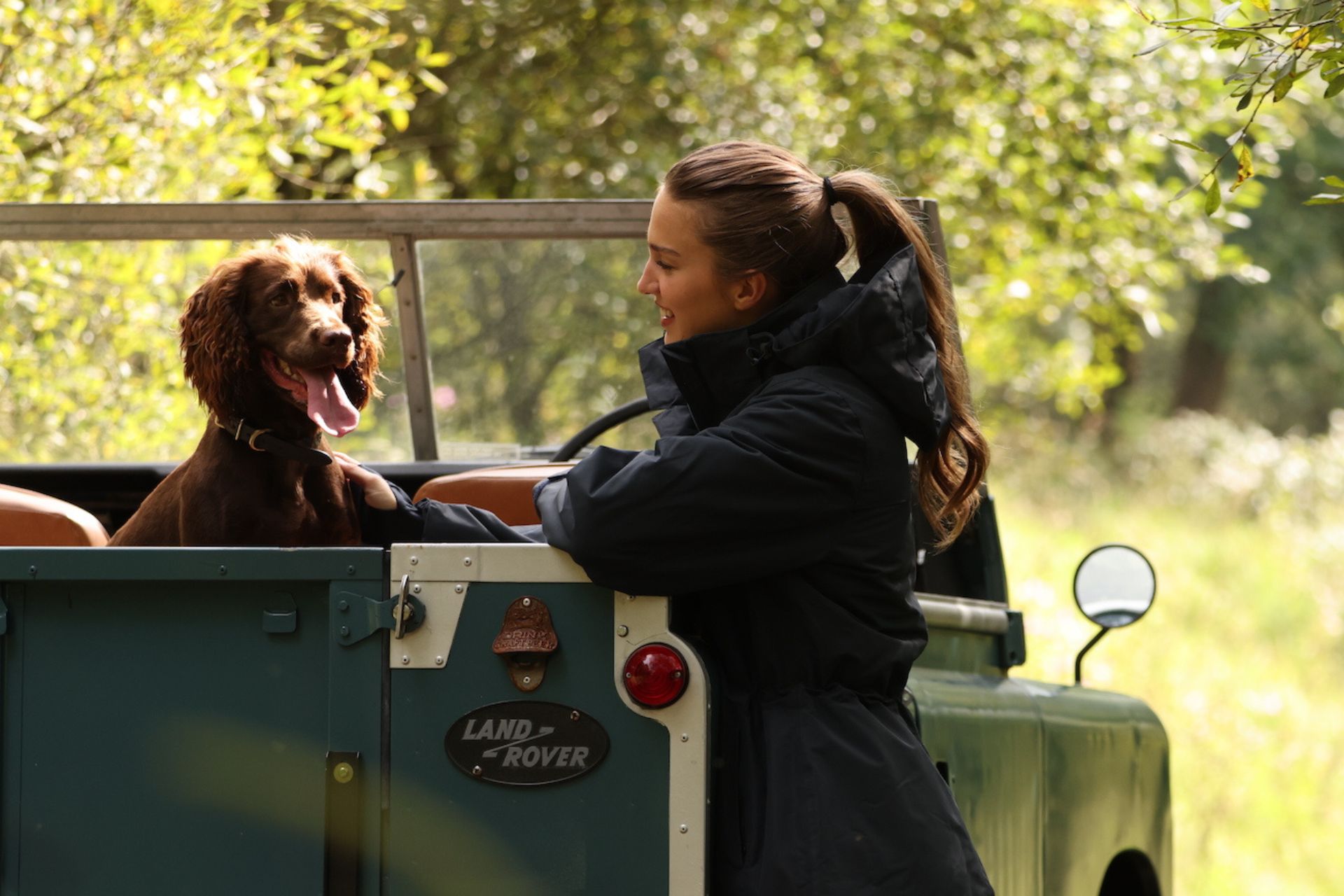 Dog sitting in Land Rover with woman beside. 