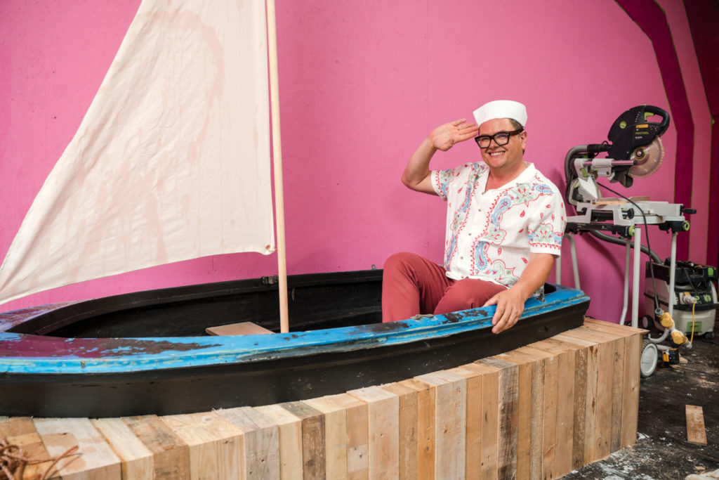 Alan Carr in a boat on a pink background