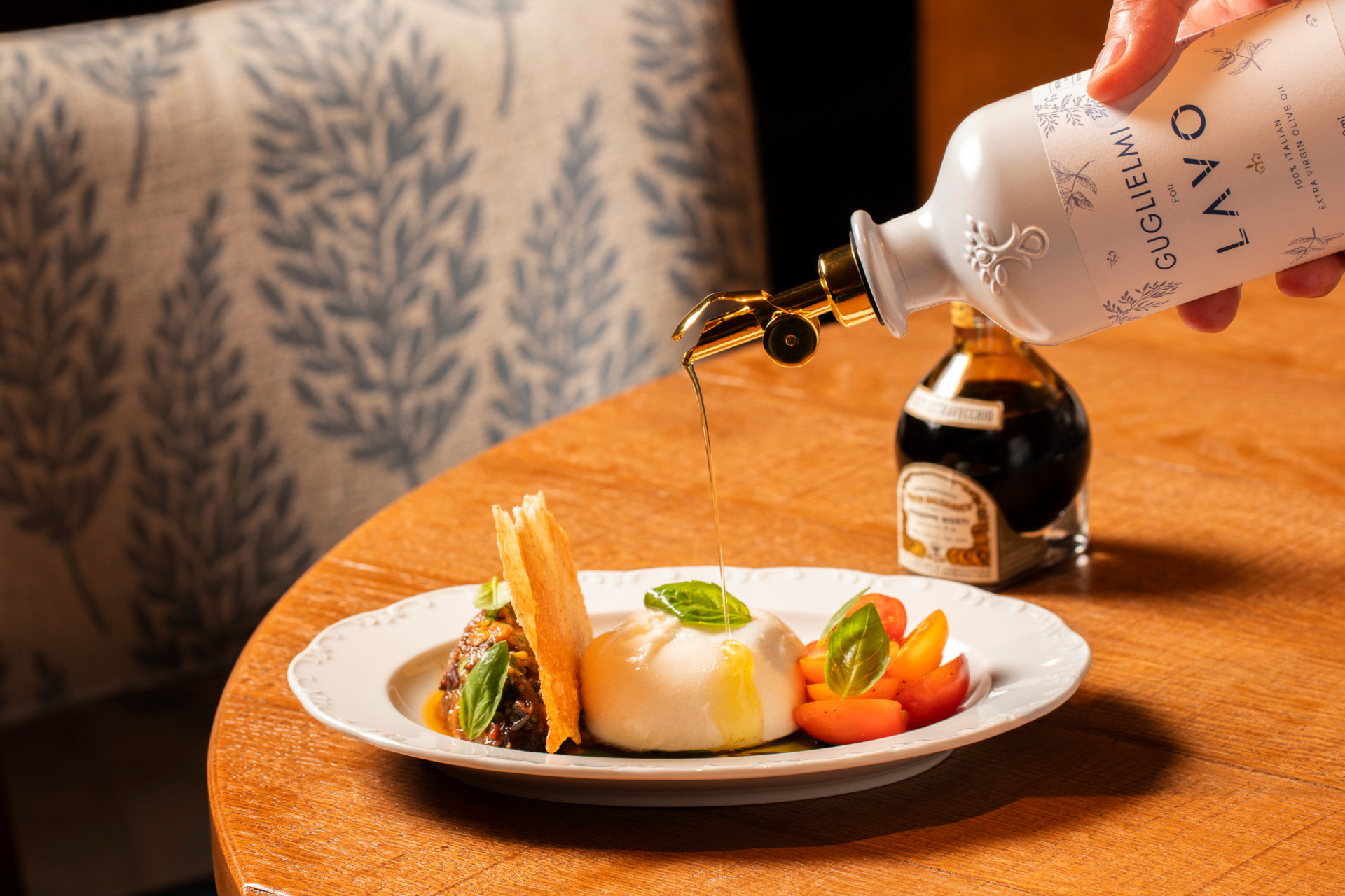 Burrata dish on plate, being drizzled with basil oil