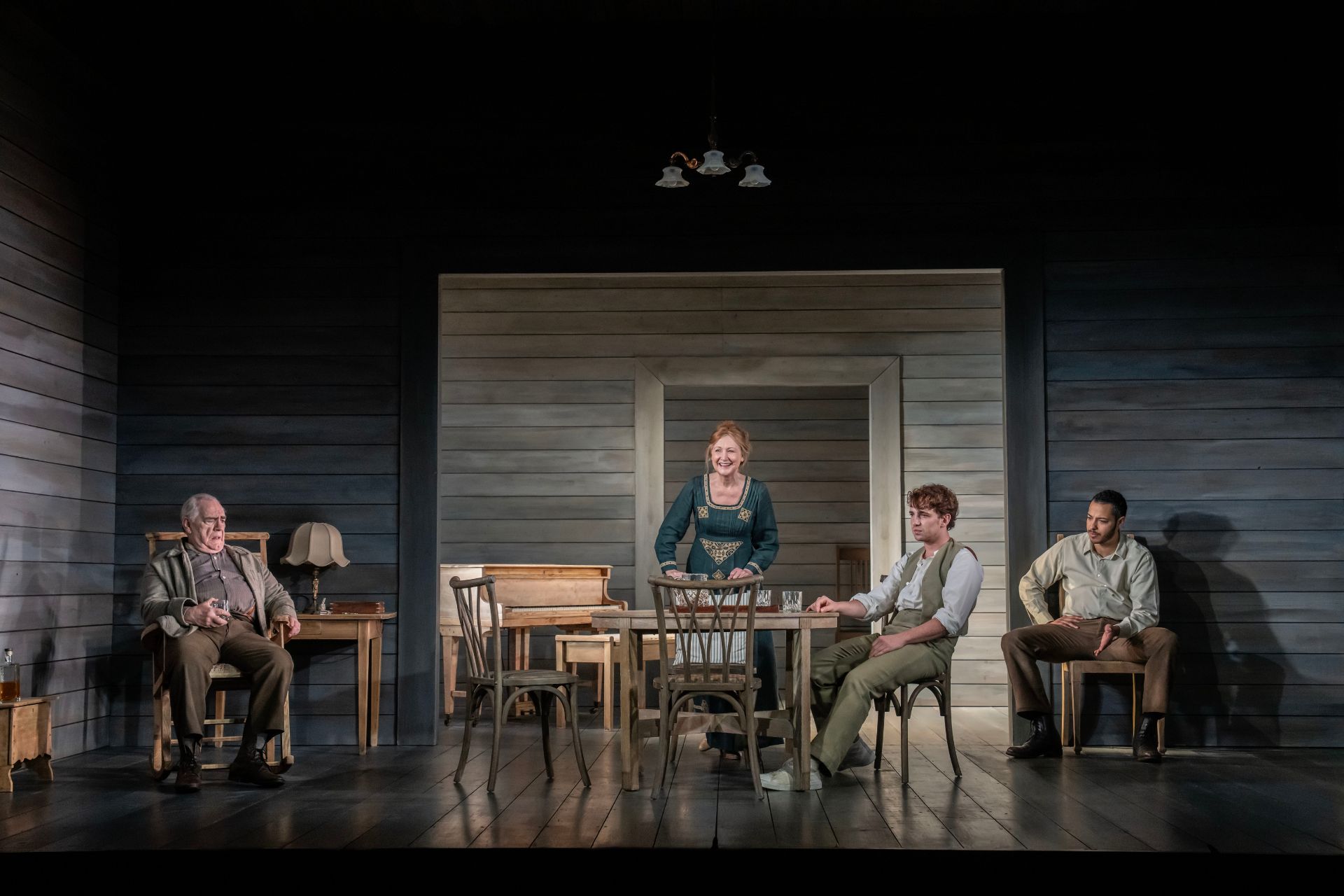 The cast of Long Day's Journey Into Night, all sitting in wooden chairs around a dining table.