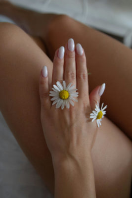 Hand with white nails and a daisy between fingers and thumb