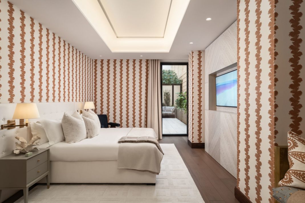 Modern bedroom with red and white wallpaper, white bed linen and a floor-to-ceiling glass door onto an outside terrace.