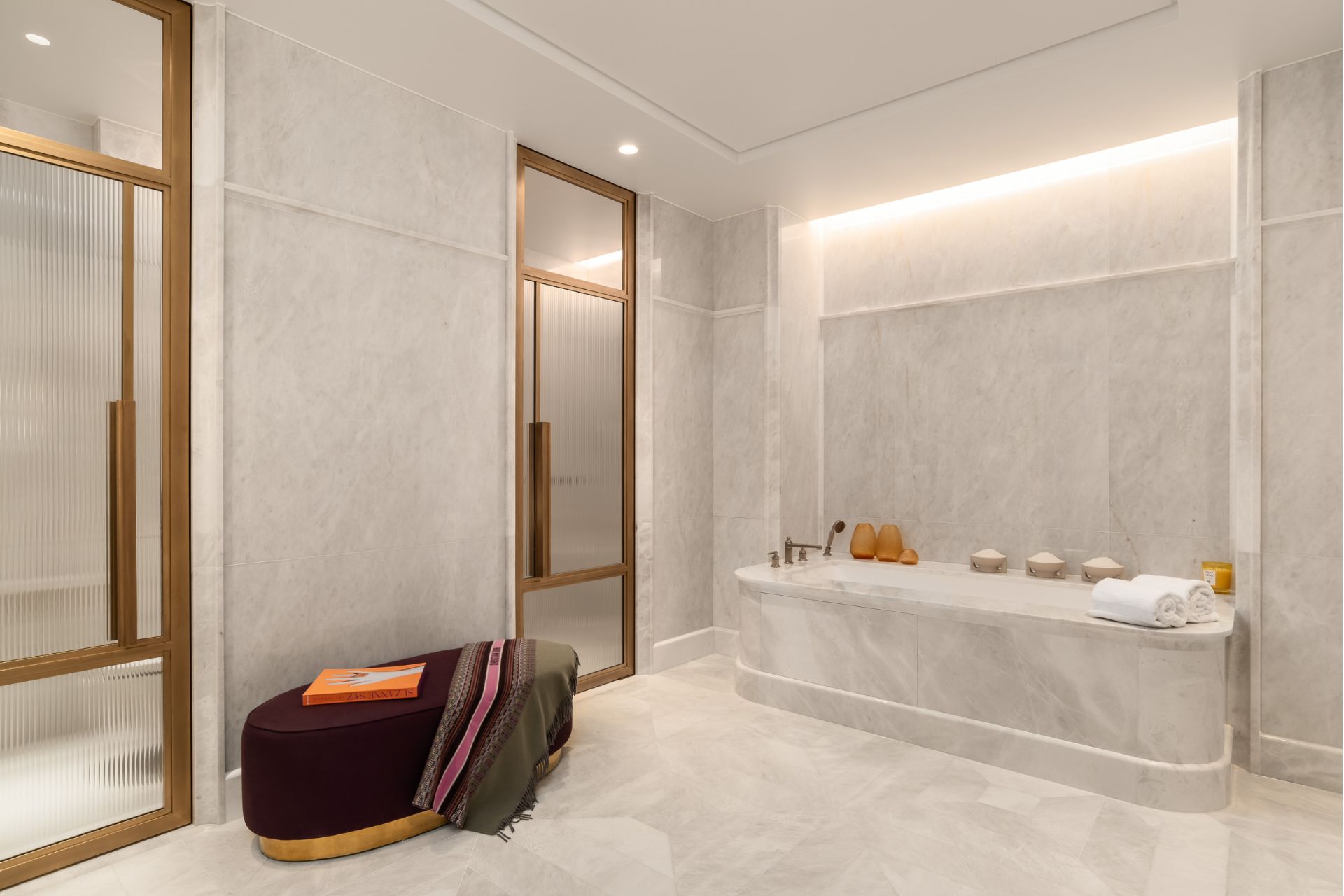 Marble bathroom with large bathtub and a velvet stool.