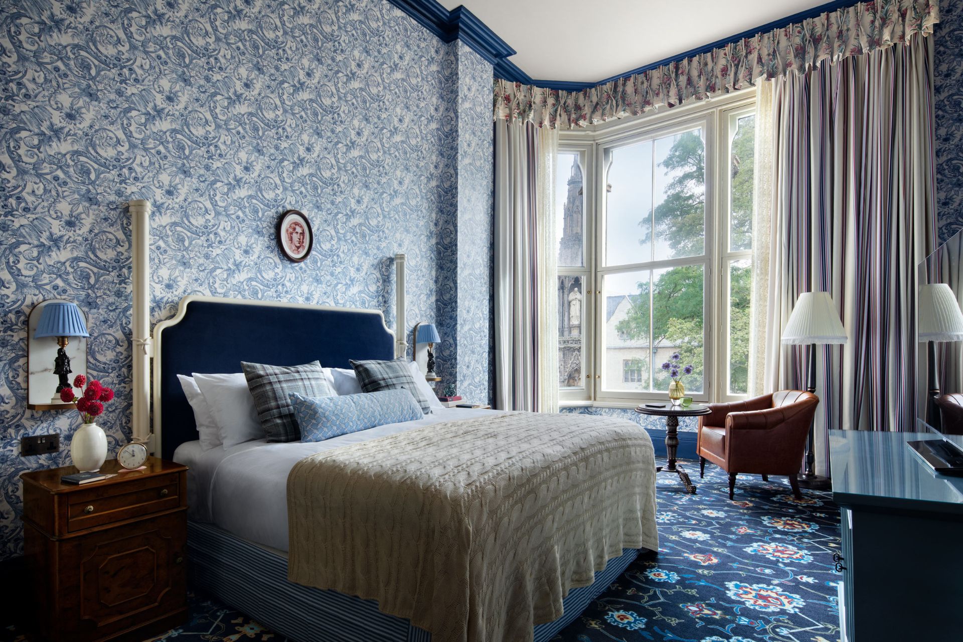 Hotel bedroom with blue floral wallpaper, clashing blue carpets and white bed linen.