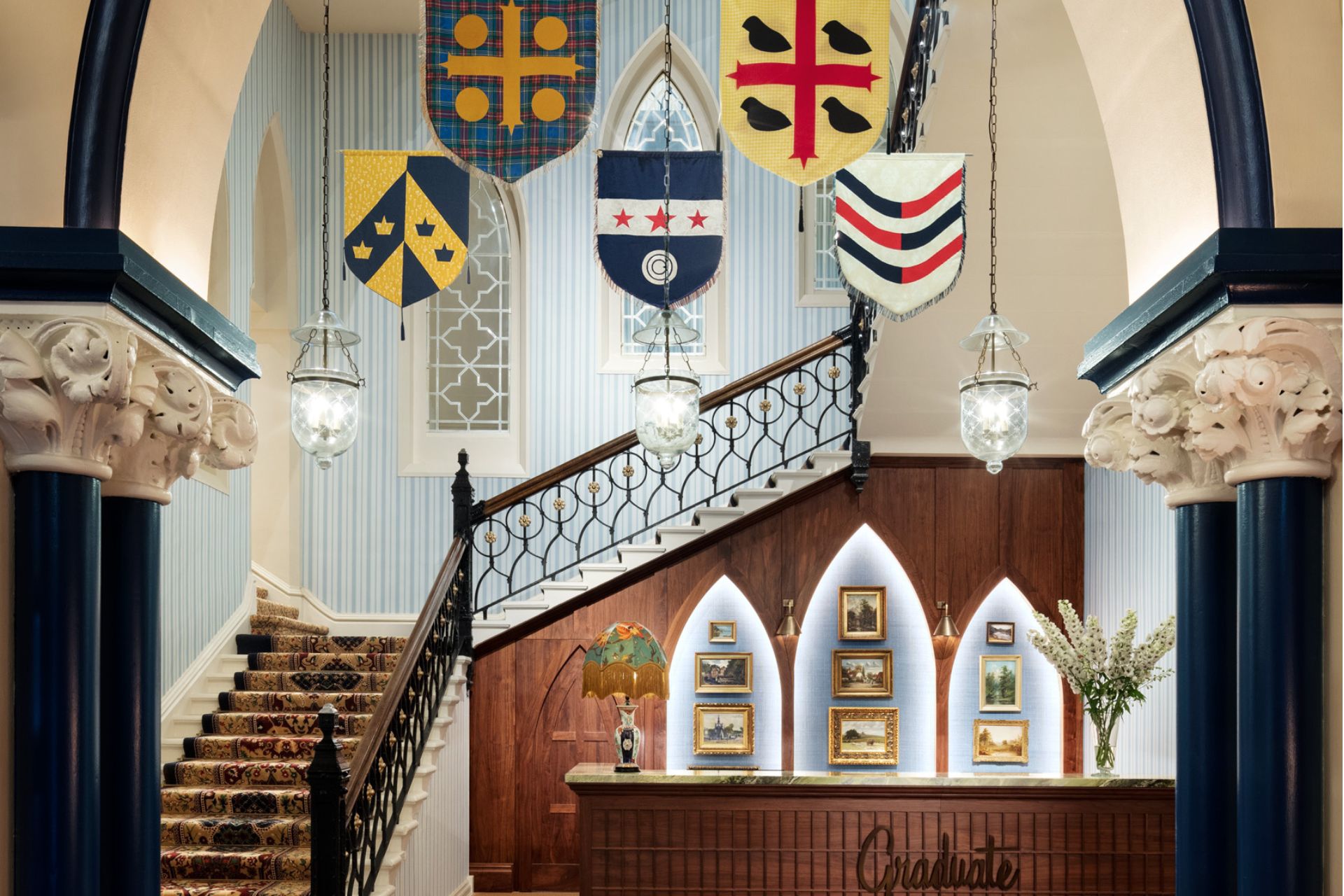 Lobby at The Randolph Hotel, with a dark wooden staircase and desk and a tapestry of Oxford college crests.