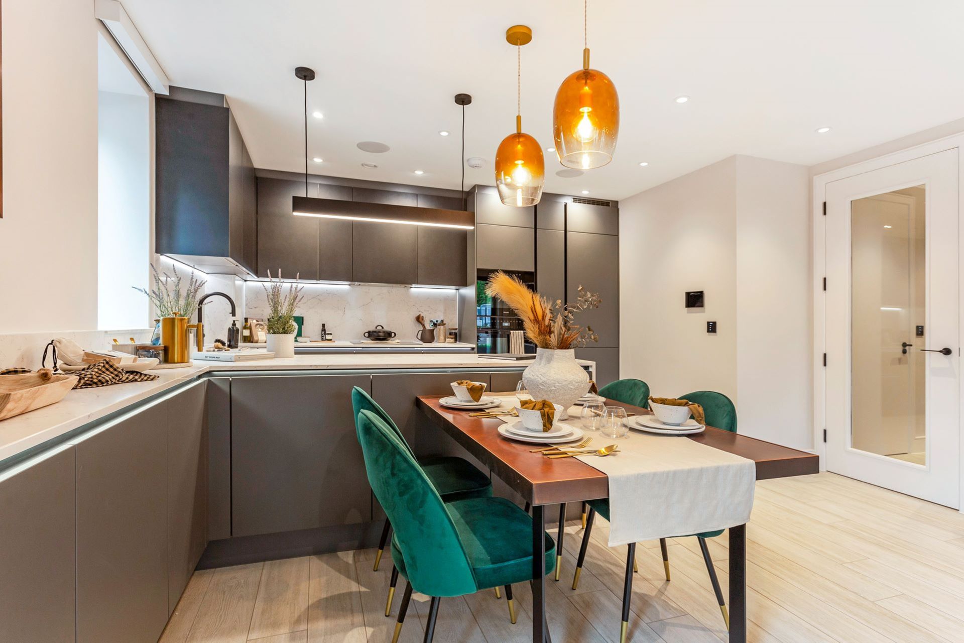 Show apartment with grey modern kitchen, white dining tale and green velvet chairs