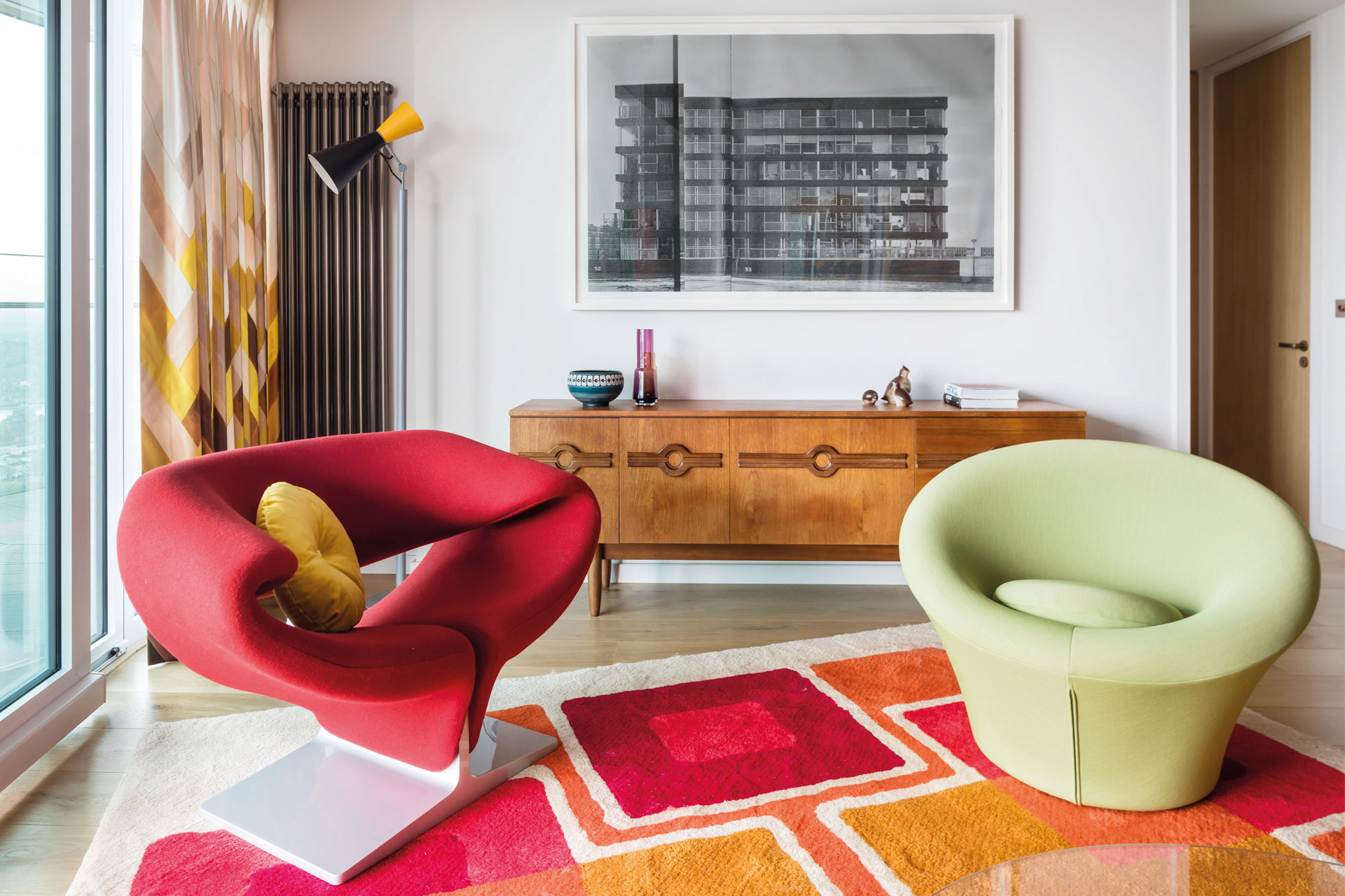 A red ribbon chair on a geometric rug alongside the mushroom chair, both designed by Pierre Paulin