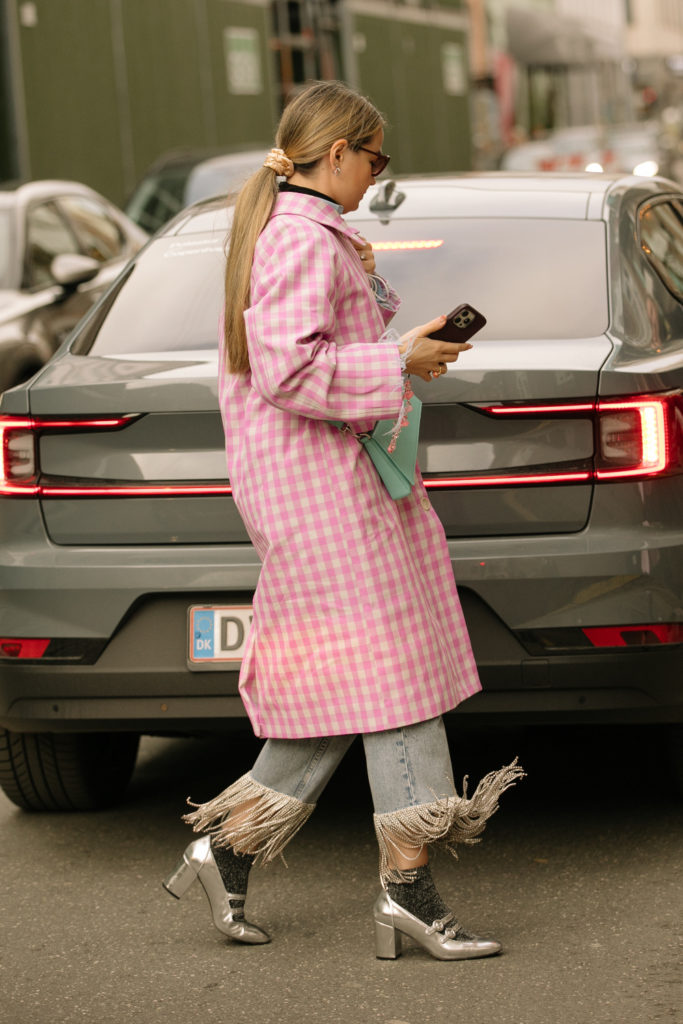 Woman with slick back ponytail wearing pink coat, jeans and silver shoes