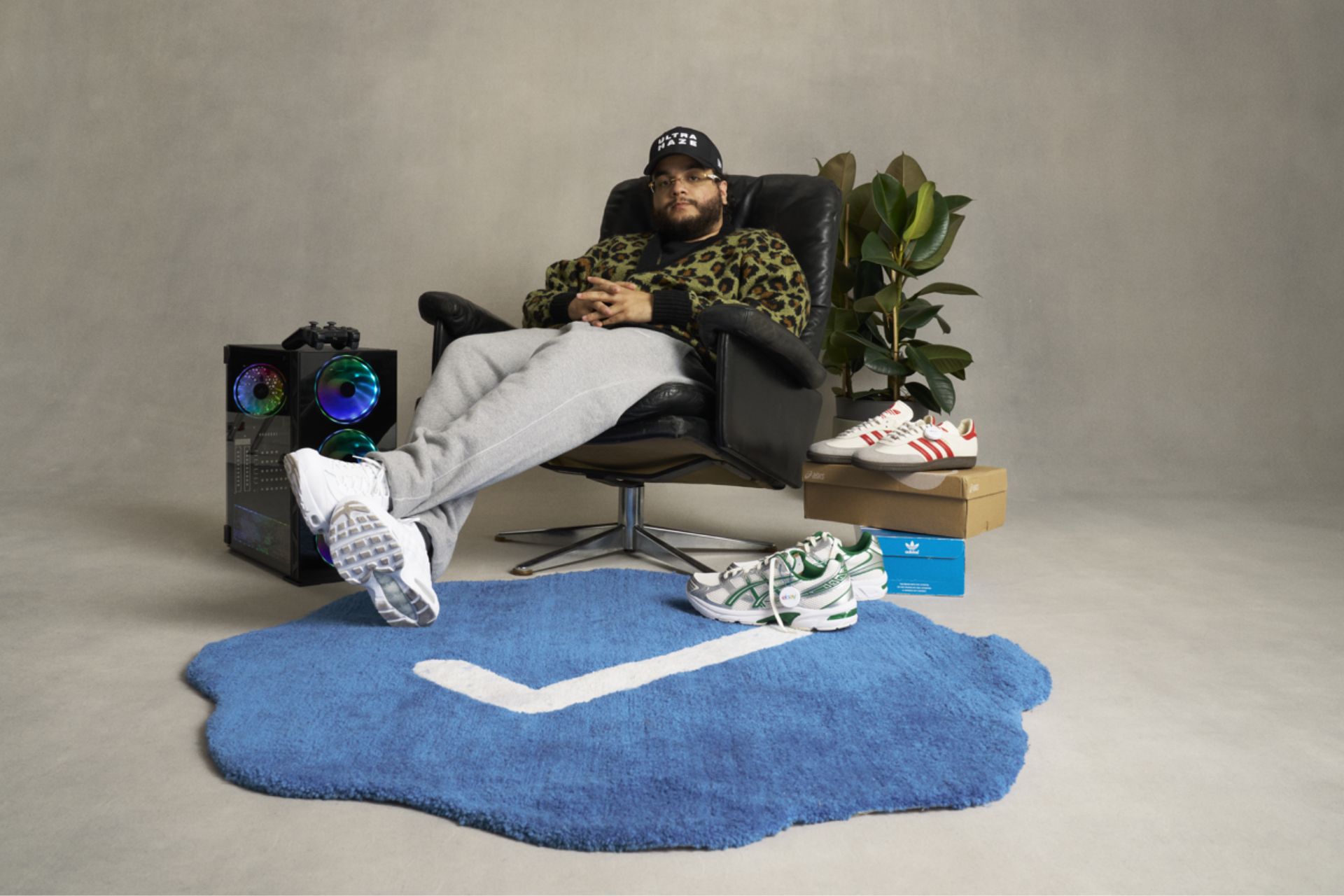 Alhan Gencay sitting in a wooden armchair next to a potted plant and various pairs of sneakers.