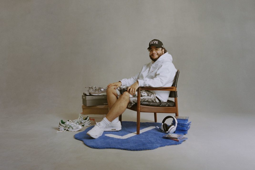 Alhan Gencay sitting in a wooden armchair surrounded by sneakers