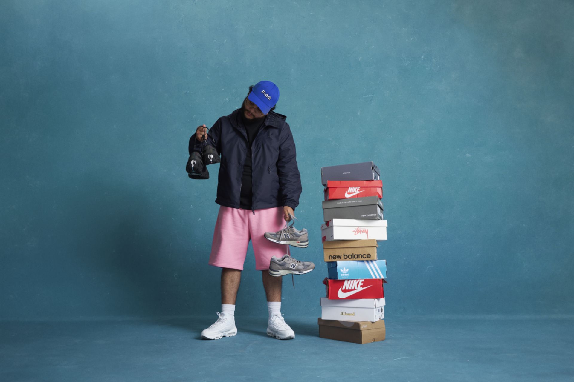 Alhan Gencay standing next to a stack of sneaker boxes, all against a blue background.