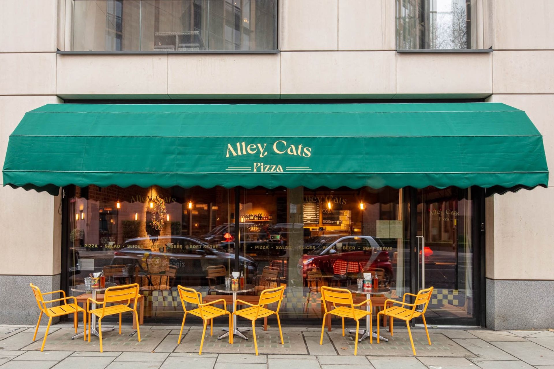 Exterior of Alley Cats, with a dark green awning and yellow outdoor furniture,