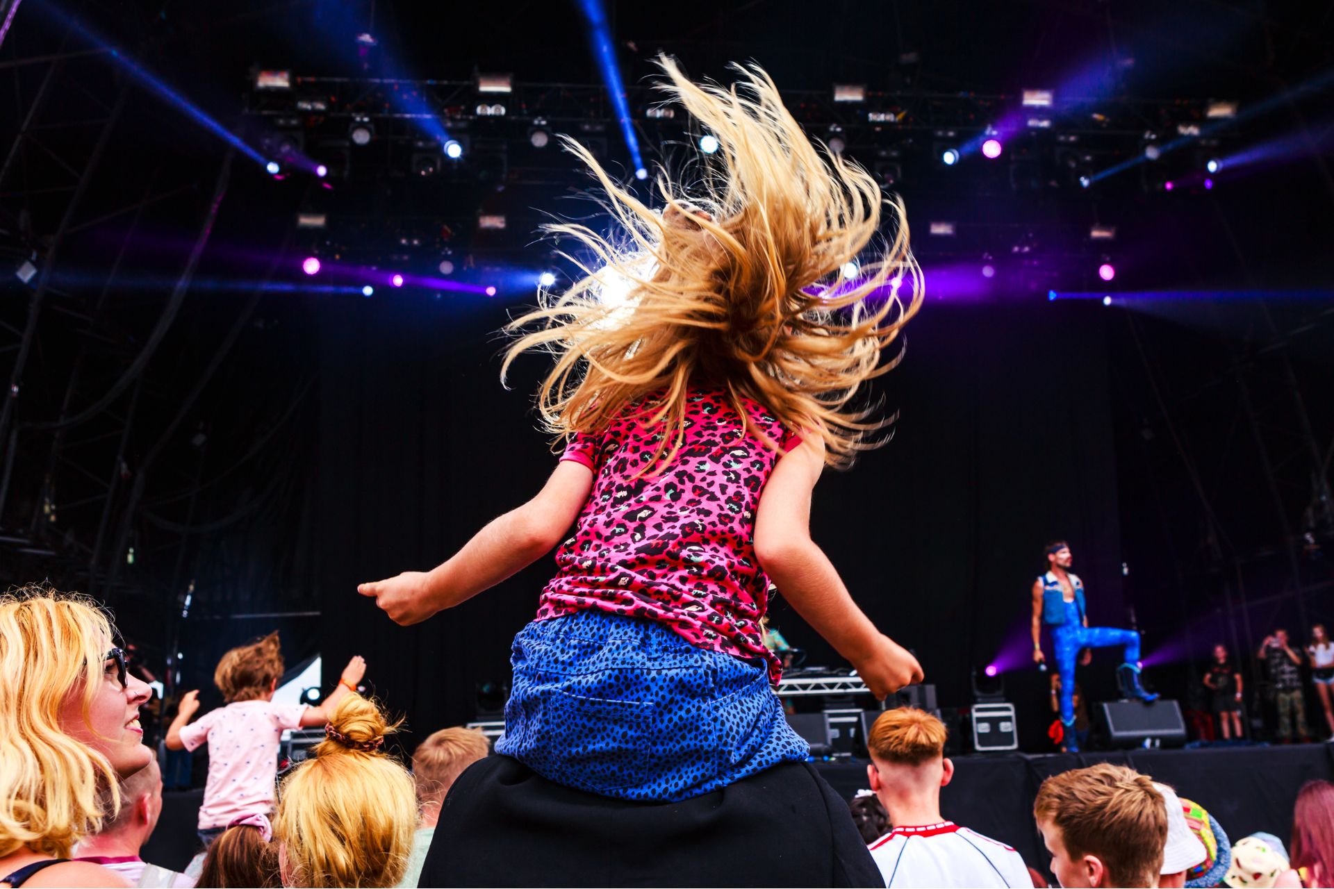 Little girl dancing on a parent's shoulders at a concert at Camp Bestival.