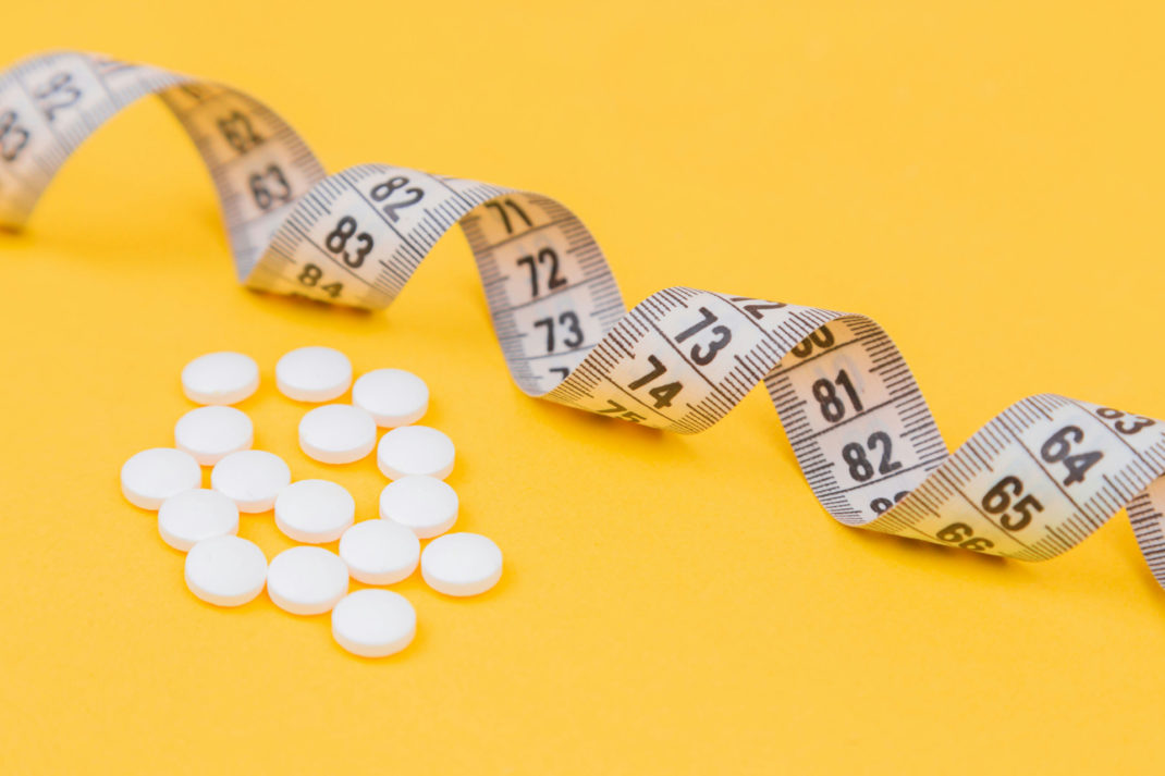 Measuring tape and pills on yellow background
