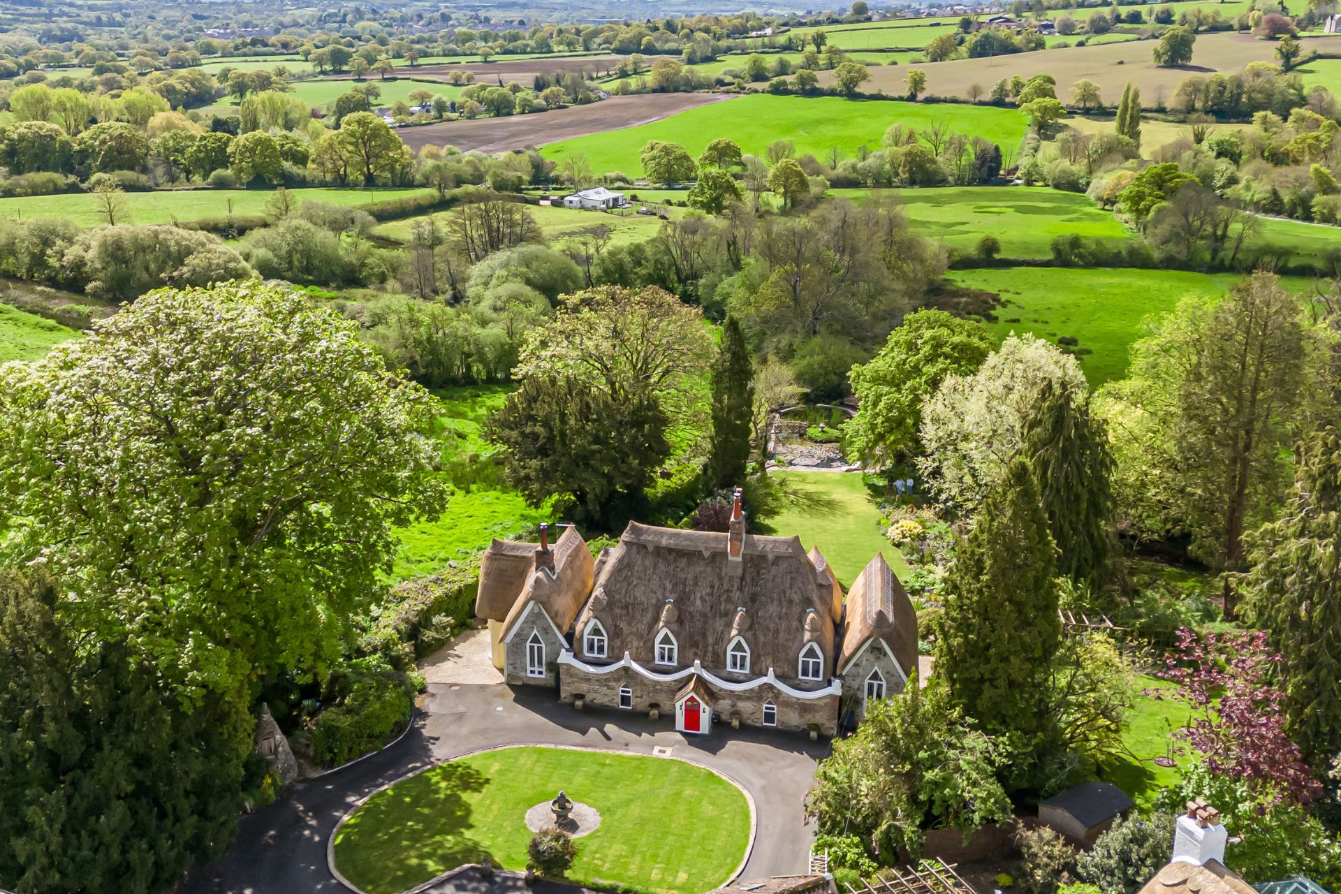 Aerial view of thatched cottage with fields around it.
