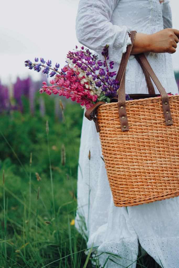 Close up of person in white dress holding raffia bag with flowers