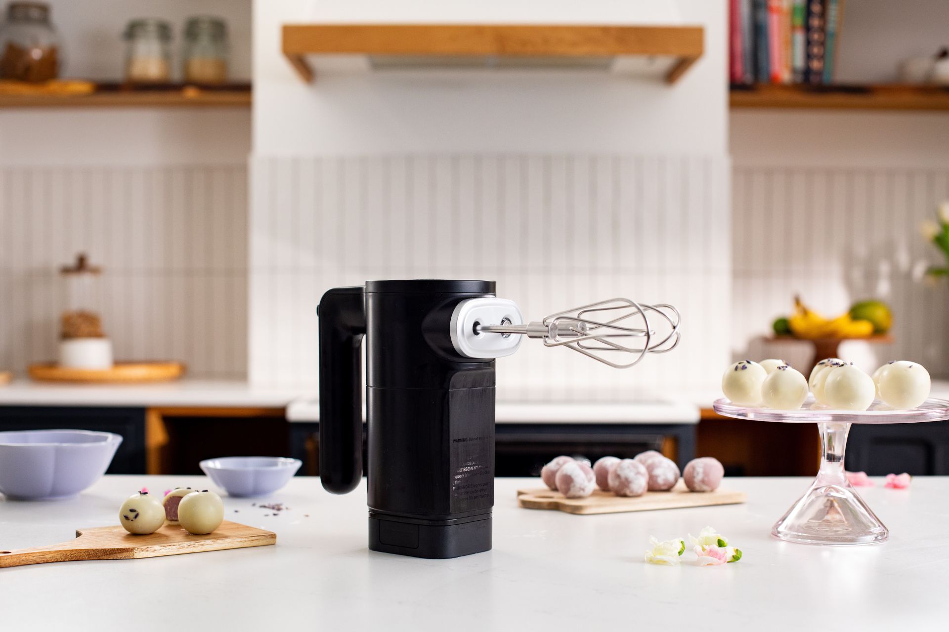 Matte black cordless KitchenAid hand mixer on a white countertop.
