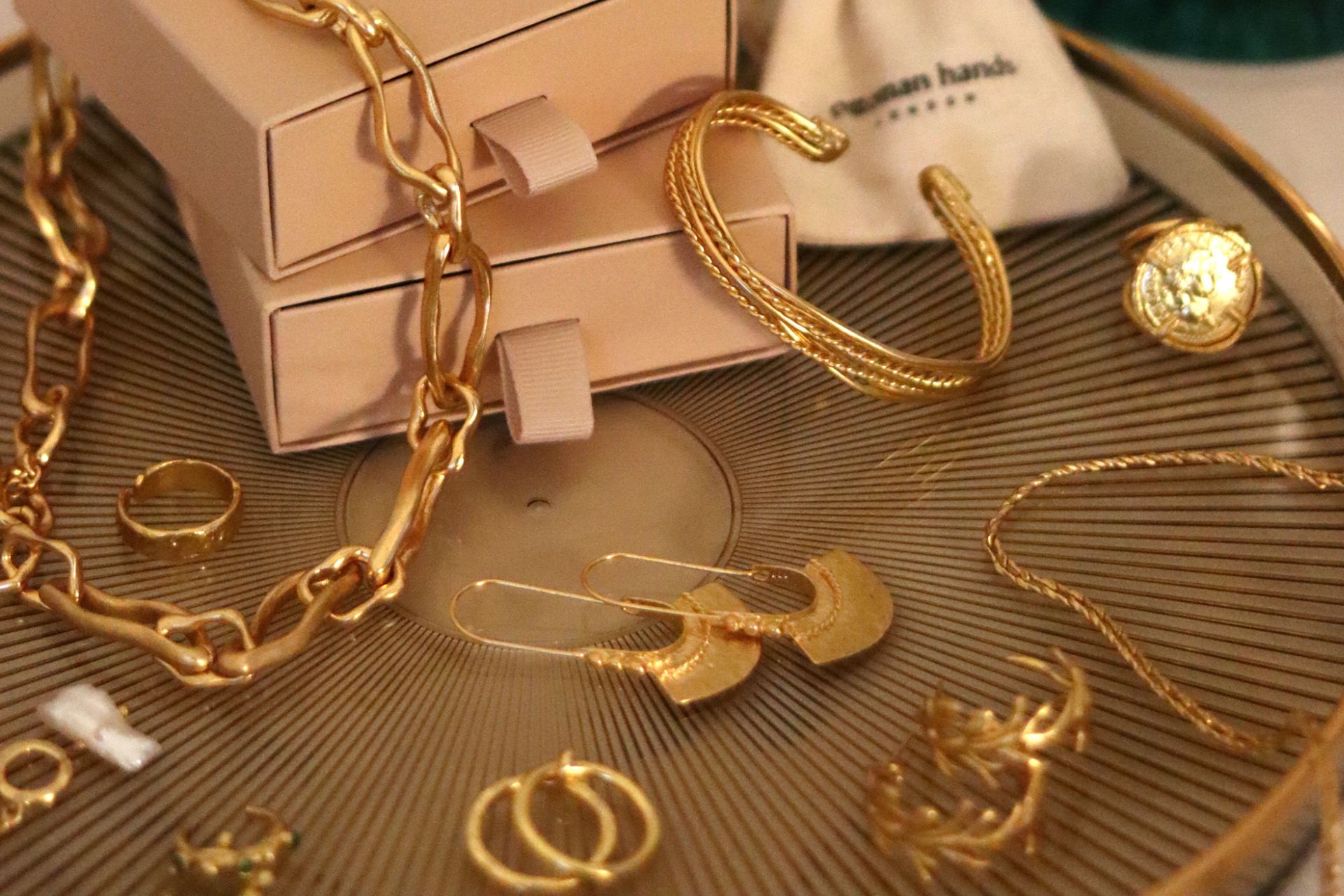 Gold earrings and rings laid out on a glass table, with pink Ottoman Hands packaging beside.