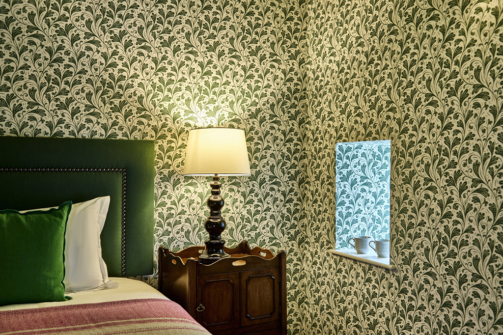 A bedroom with green leafy wallpaper