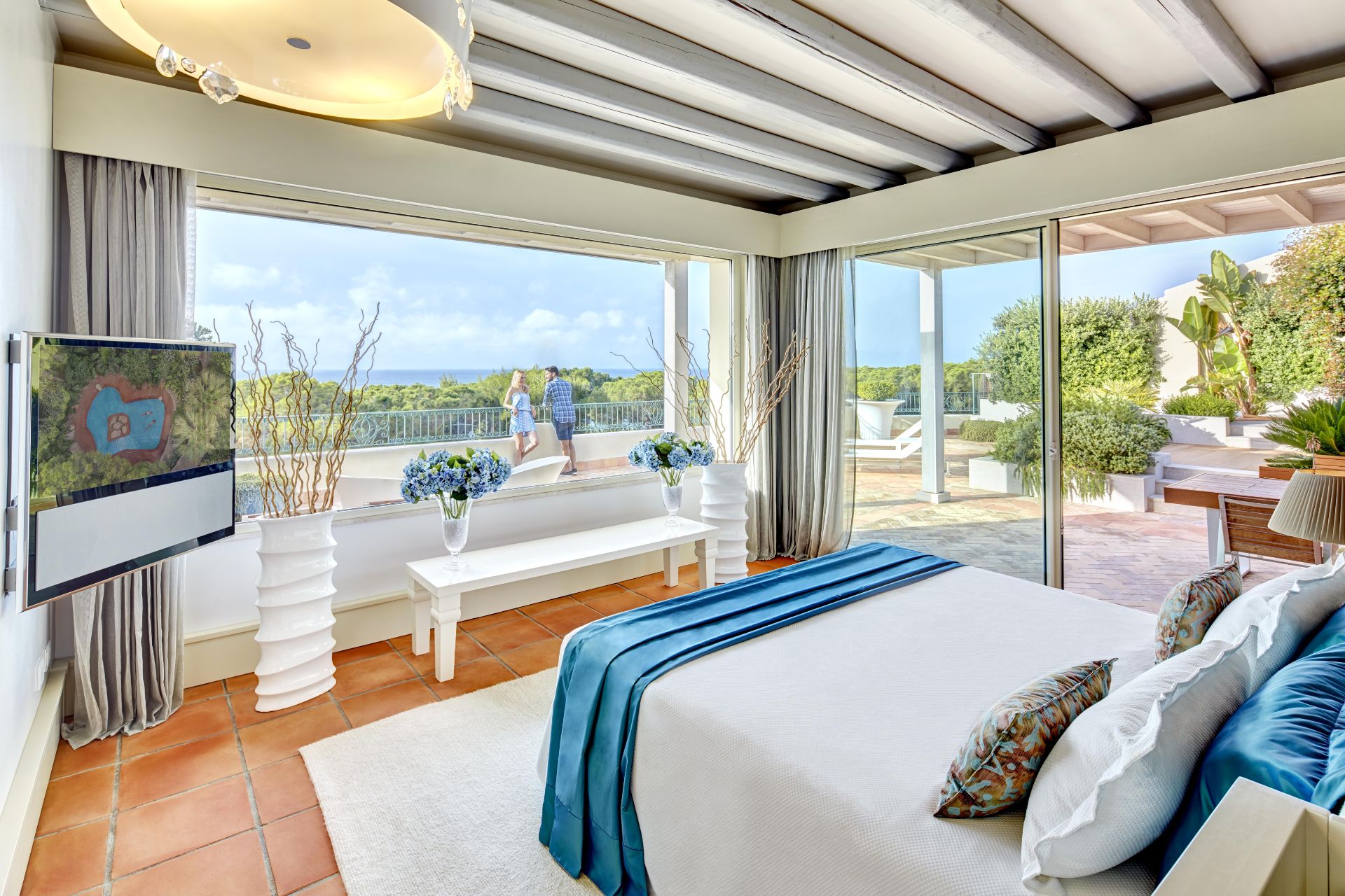Resort bedroom with blue accents and floor-to-ceilings windows overlooking the sea.