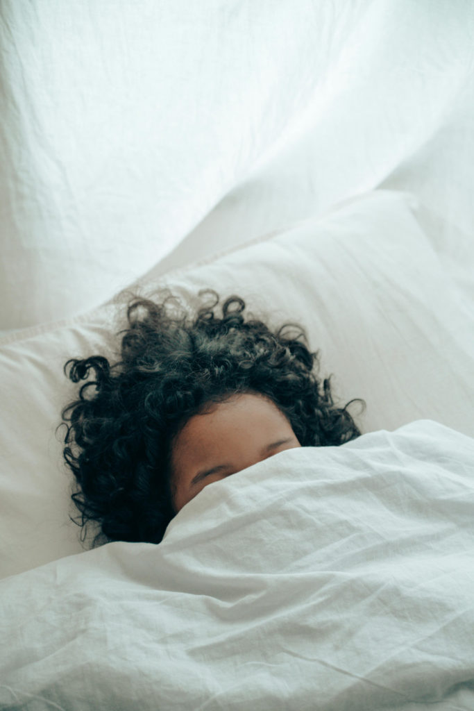 A person tucked up in bed with their hair splayed across the pillow
