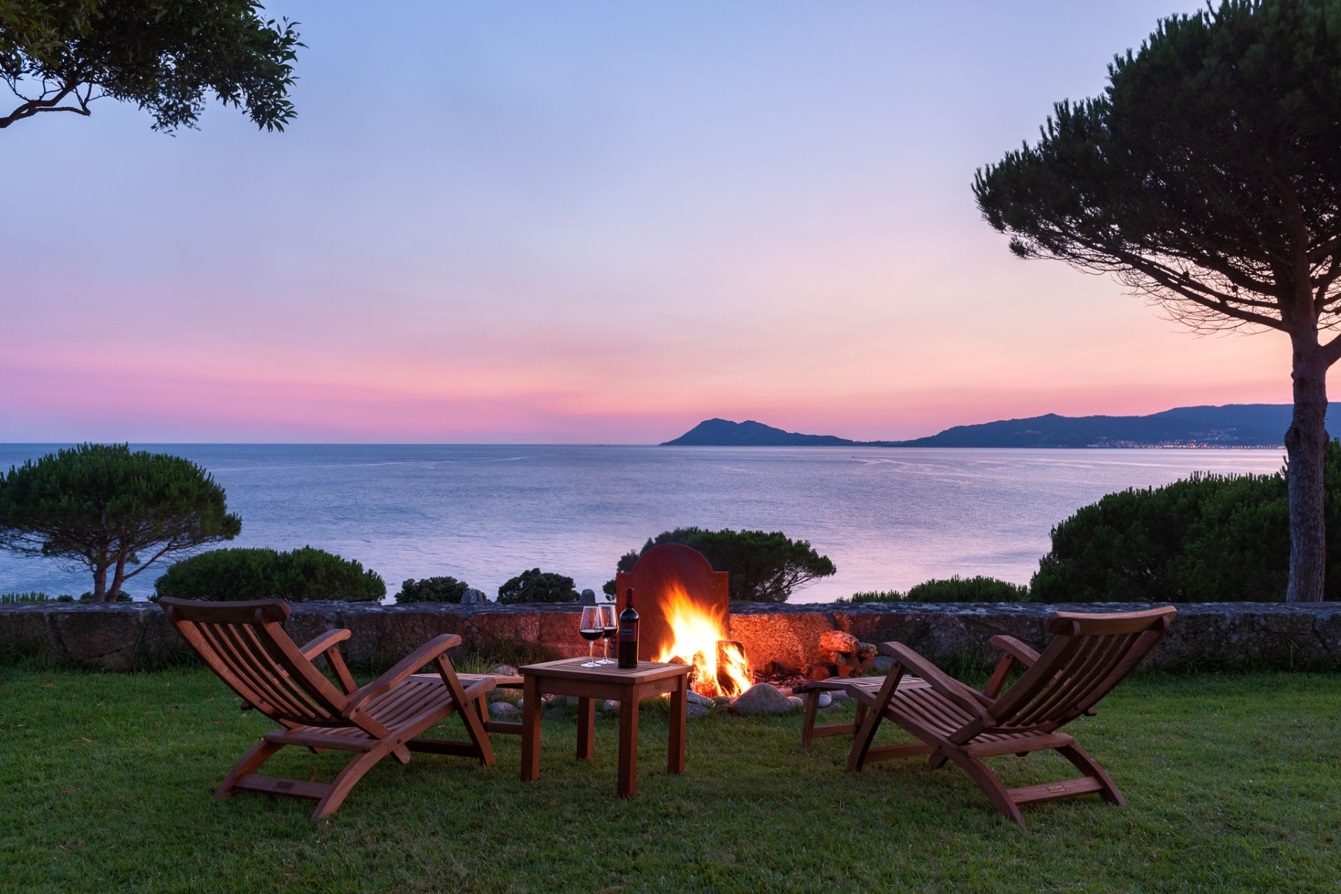 A cliffside with deck chairs and a fire, photographed at sunset.